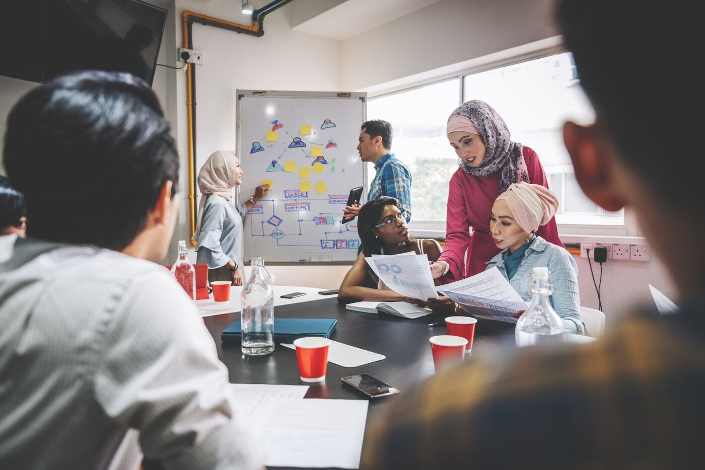 A multicultural team engaging in a dynamic brainstorming session around a conference table with documents in hand.