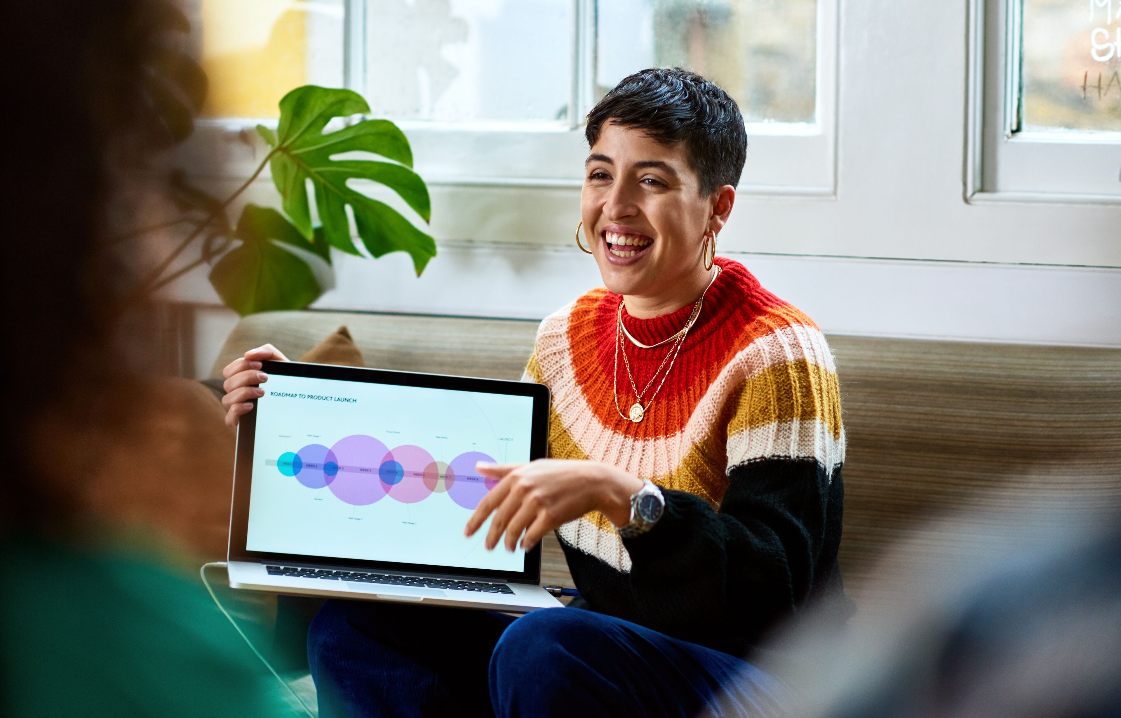 Profesional sonriente muestra una hoja de ruta empresarial colorida en una laptop a un colega no visible.