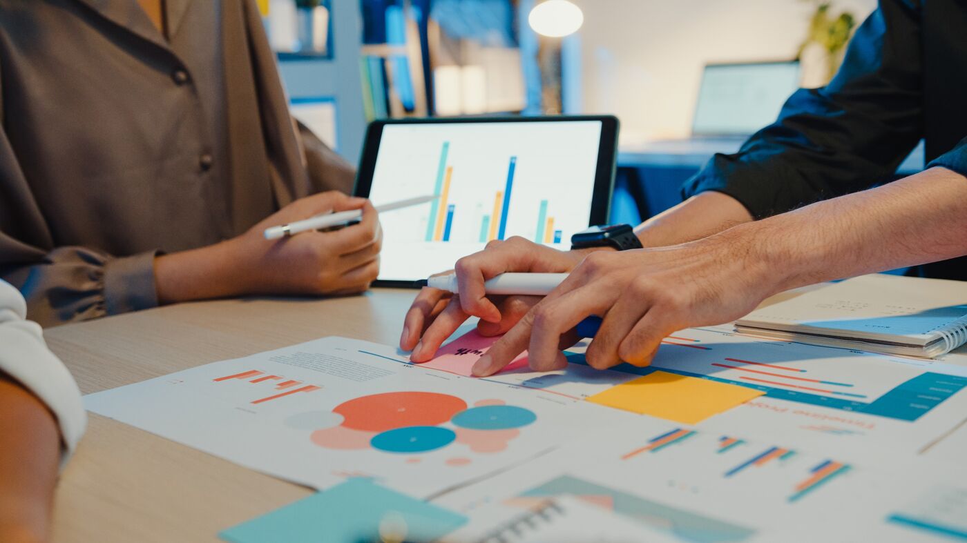 A group of professionals engaged in a data analysis session, examining various charts and graphs on paper and digital devices.