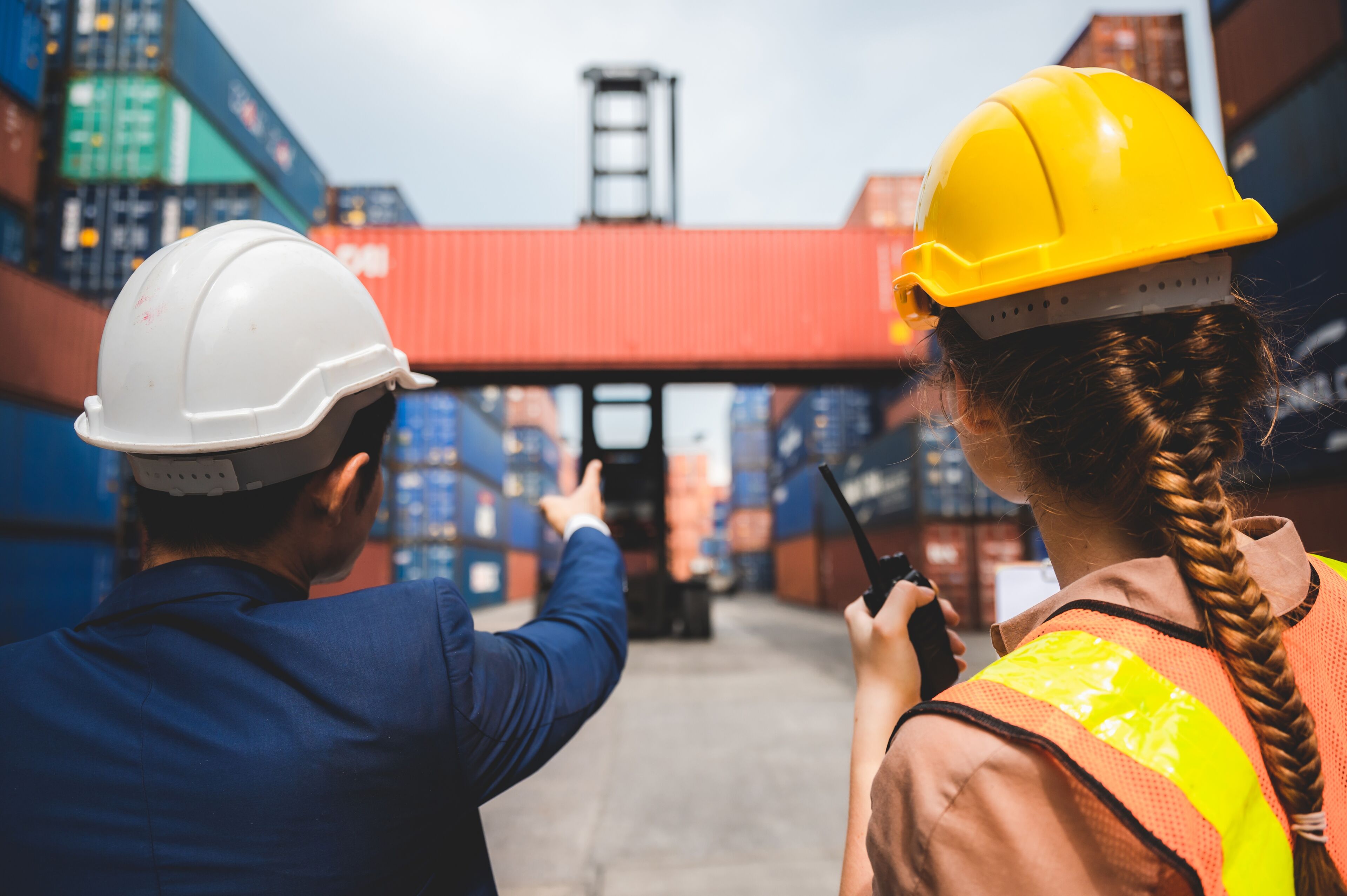 Experts en logistique avec casques et gilets haute visibilité supervisent les opérations de conteneurs dans un port commercial.