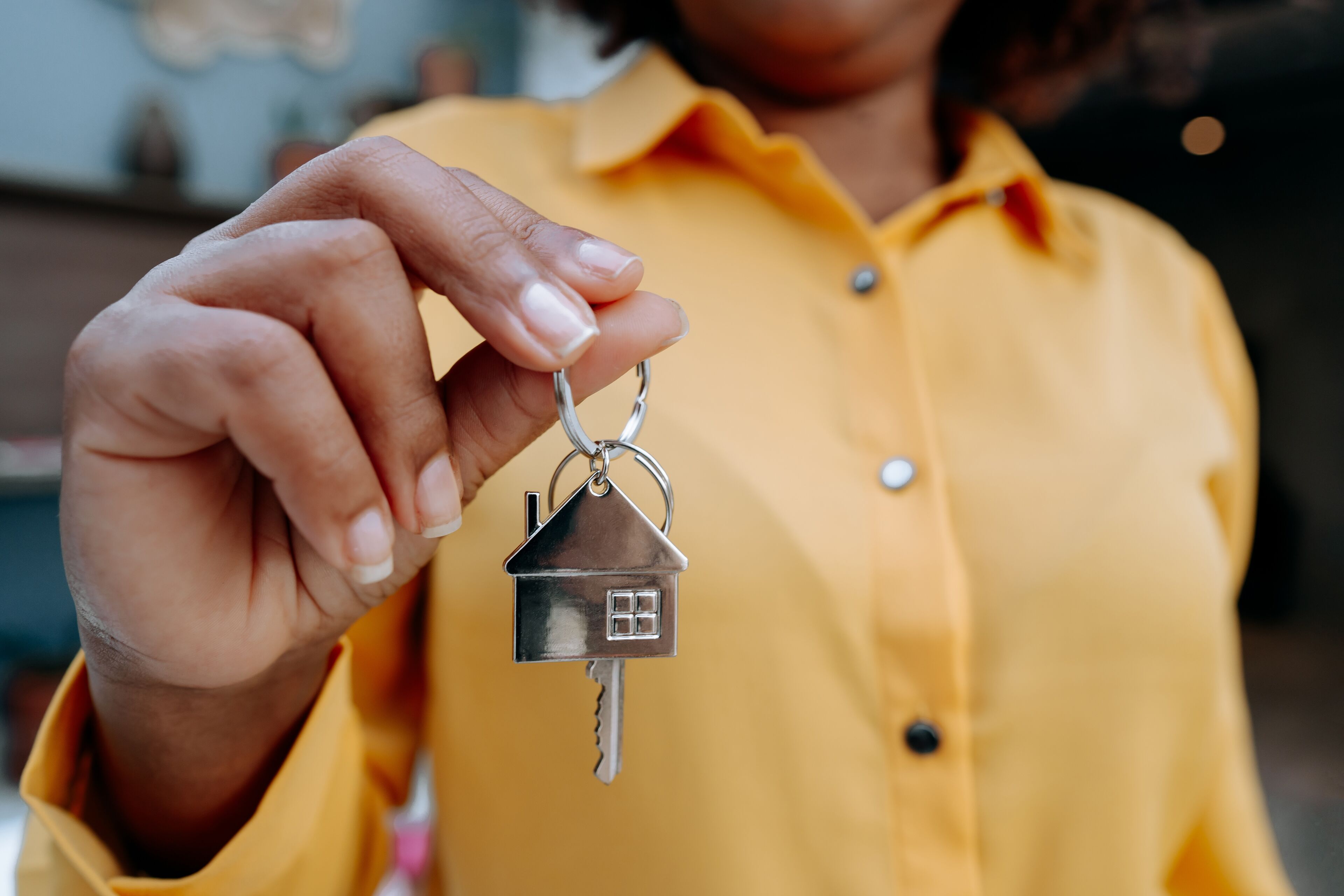 A close-up of a person's hand presenting a key with a house-shaped keychain, symbolizing new homeownership.