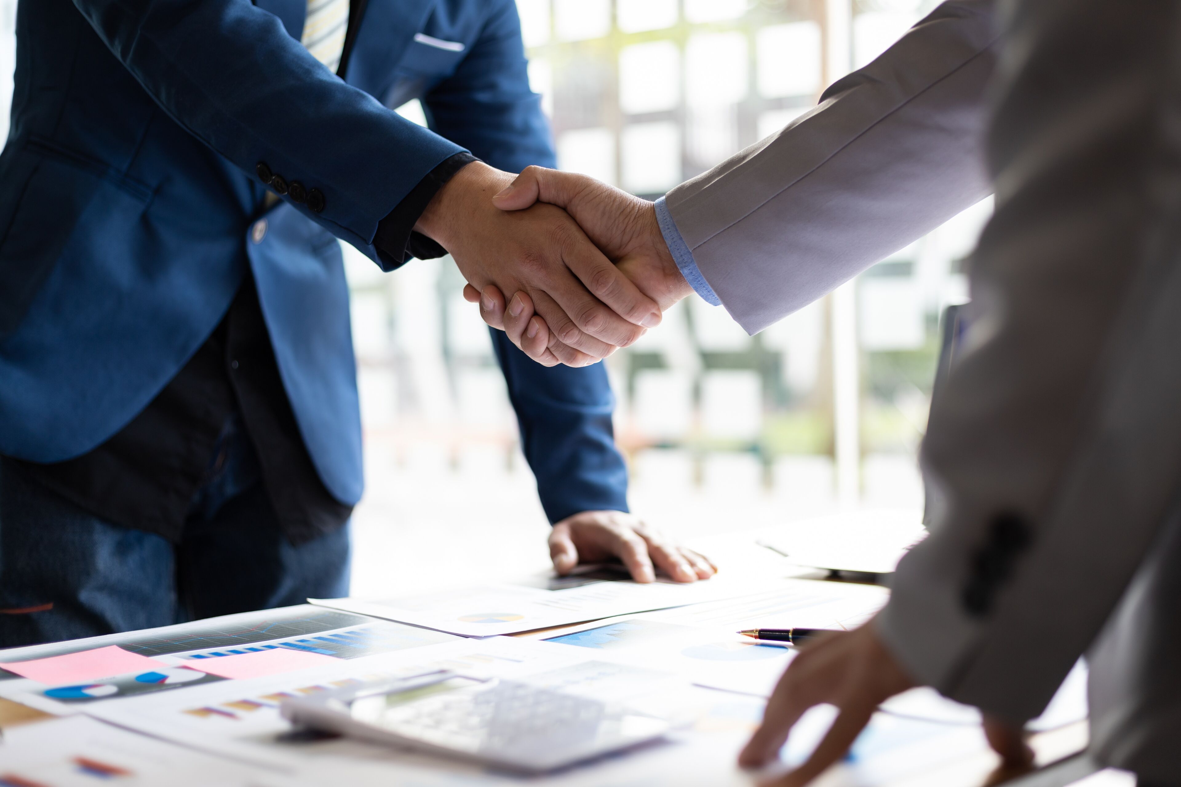 Two professionals sealing a deal with a handshake over a table with documents and a laptop.