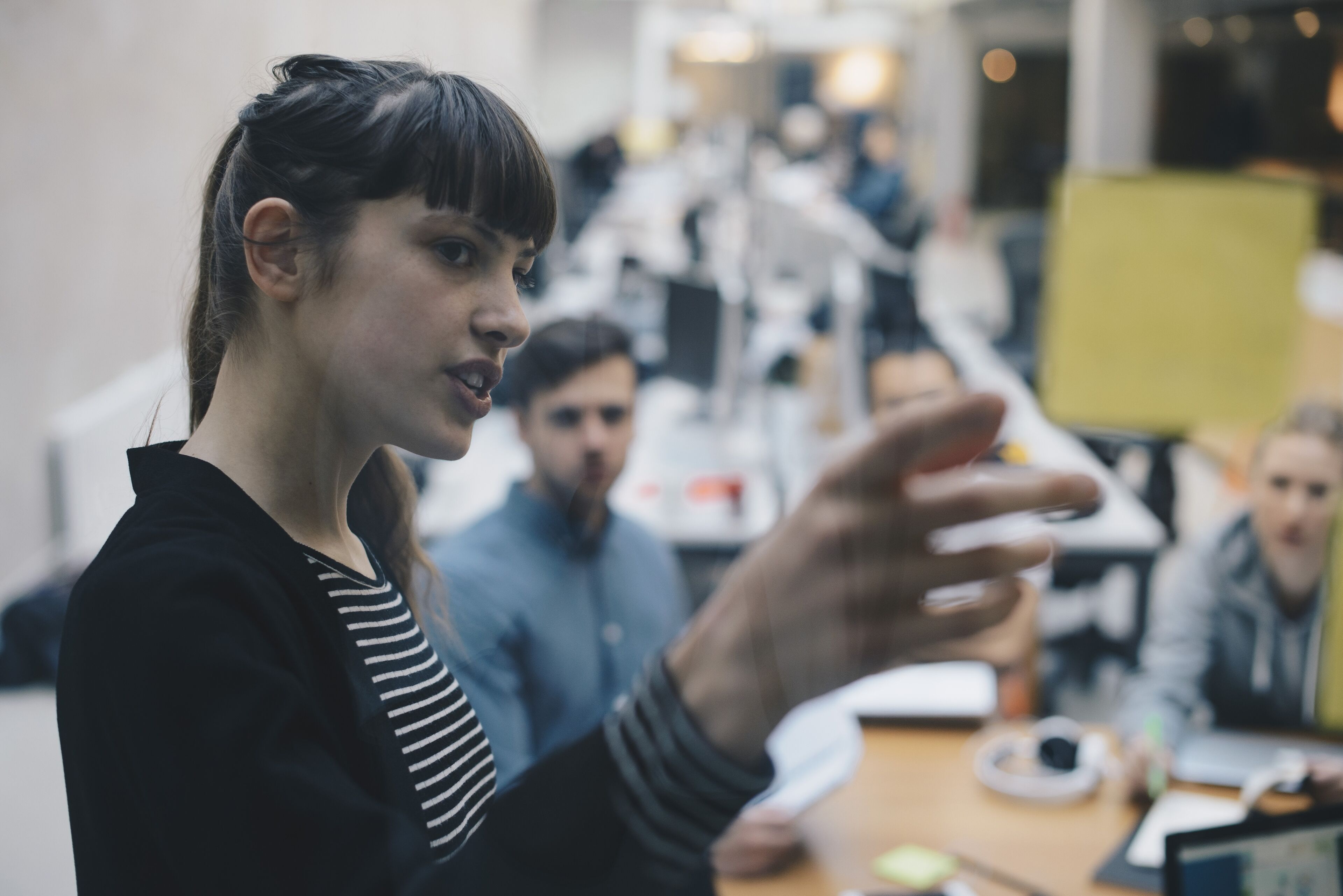 A focused businesswoman speaks to colleagues during a collaborative office meeting.