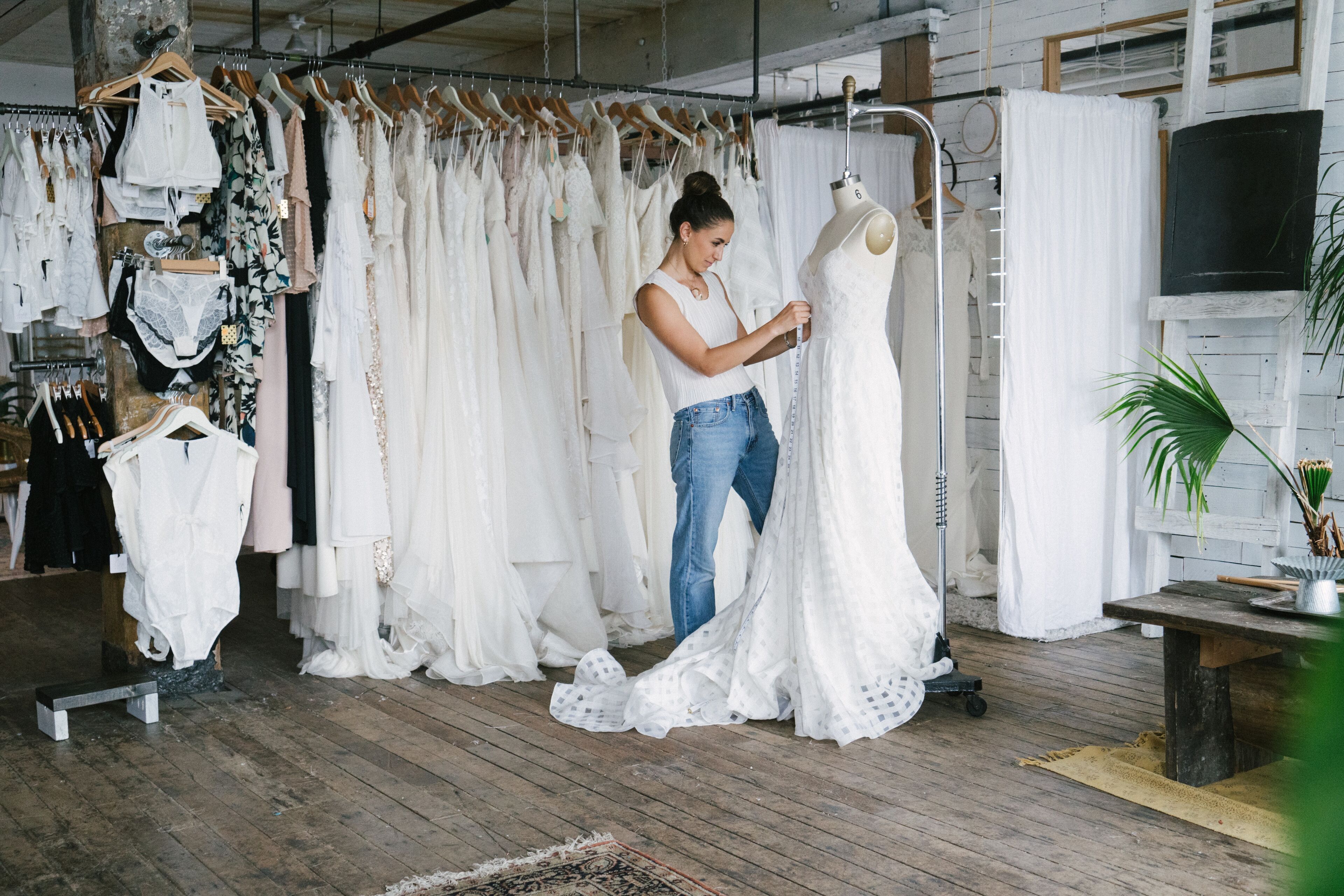 A woman tailoring a bridal gown in a boutique with various dresses in the background.