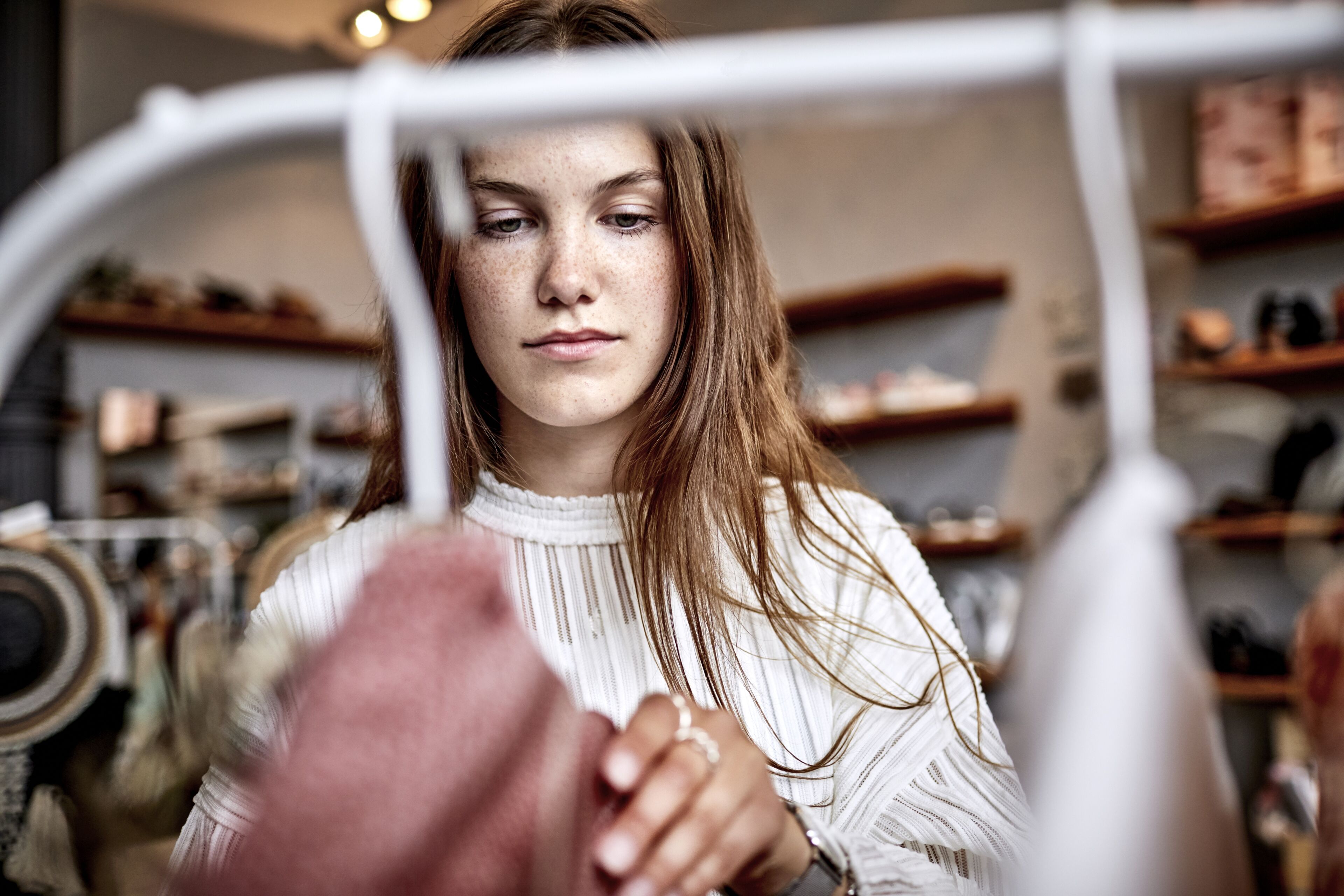 Une jeune femme examine attentivement un vêtement dans une boutique, l'expression songeuse.