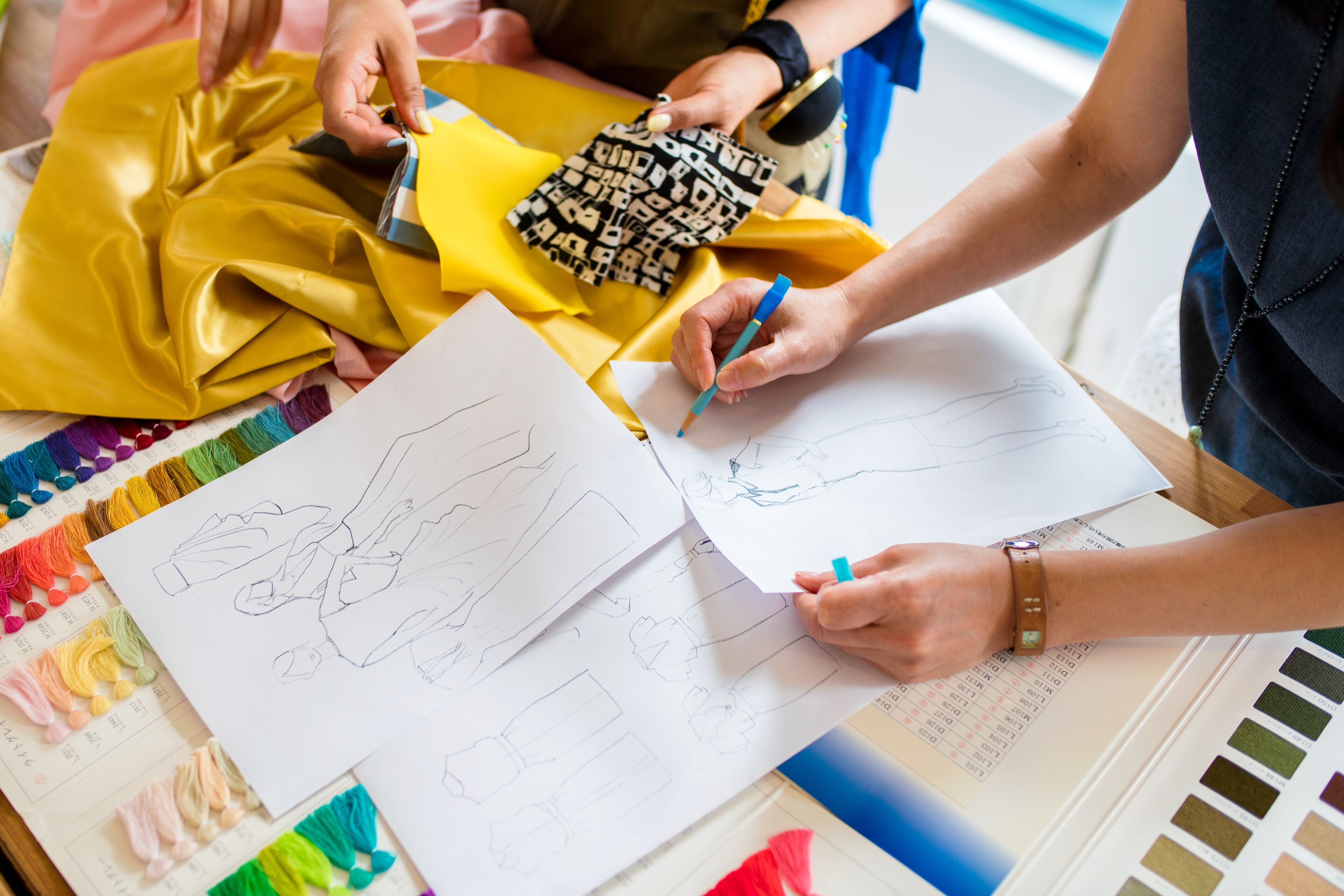 Mains dessinant des vêtements avec des échantillons de tissus et palettes de couleurs sur une table.