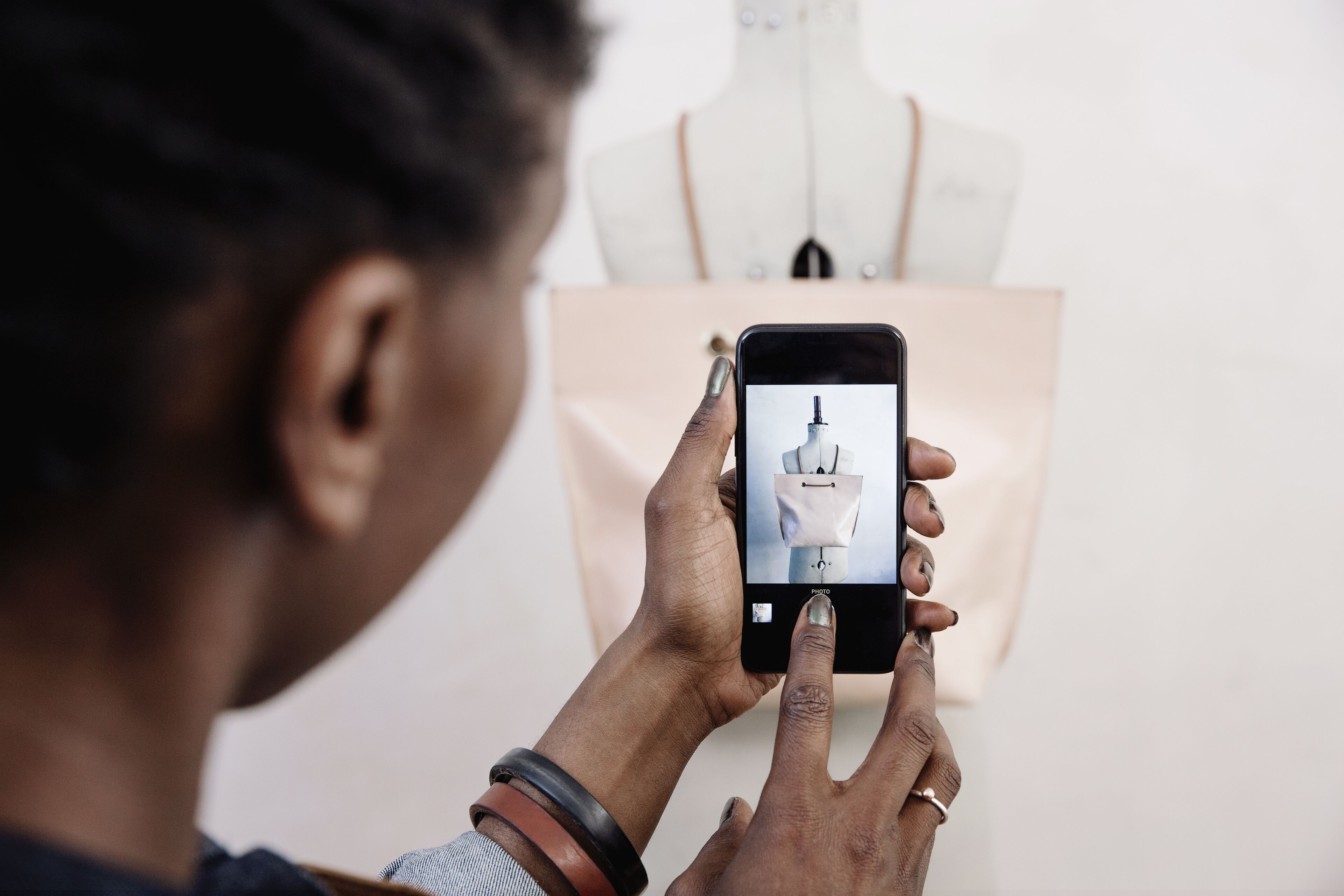 A person captures a mannequin on a smartphone, blending fashion design with digital tools.