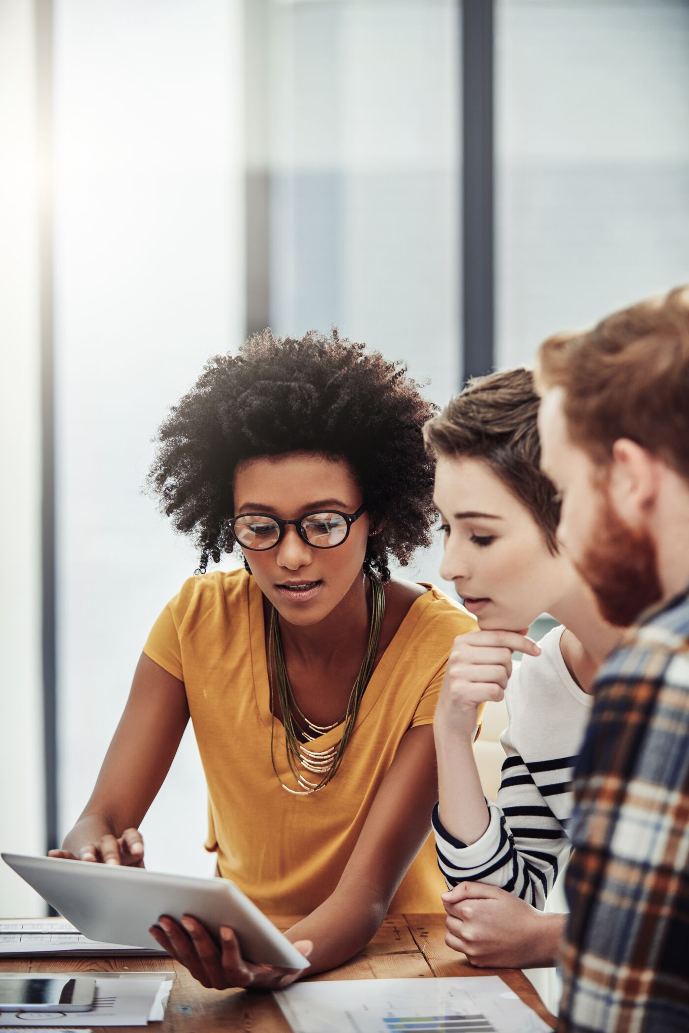 Three professionals engaging in a collaborative discussion over a digital tablet in an office setting.