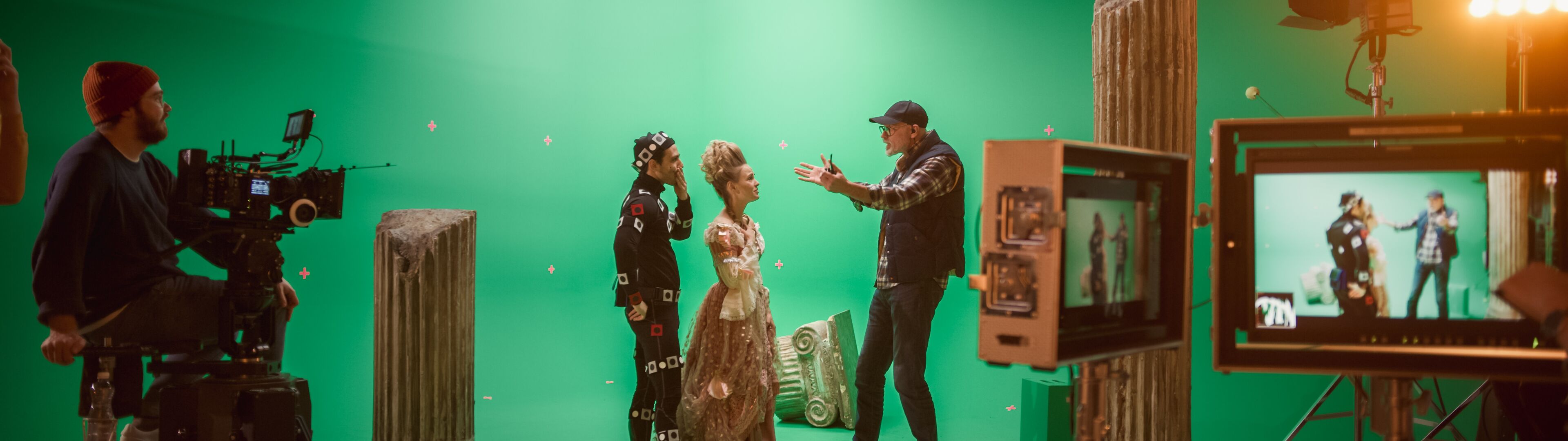 Director instruyendo actores con trajes de captura de movimiento en un set con pantalla verde, con equipo de cámara e iluminación.