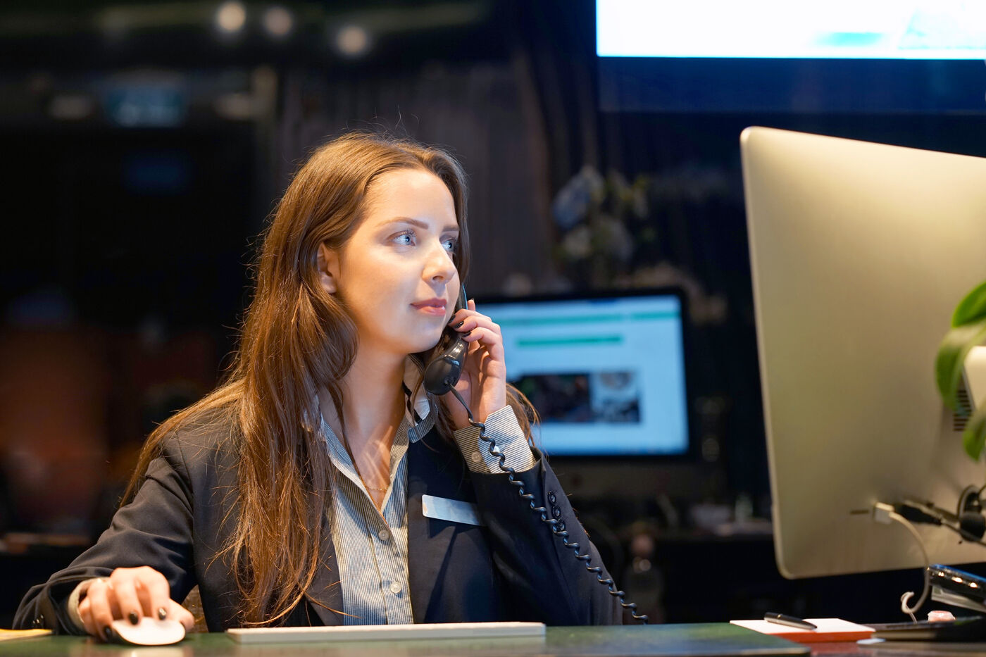 A professional receptionist at a hotel front desk is speaking on the phone, possibly assisting with a reservation or inquiry.