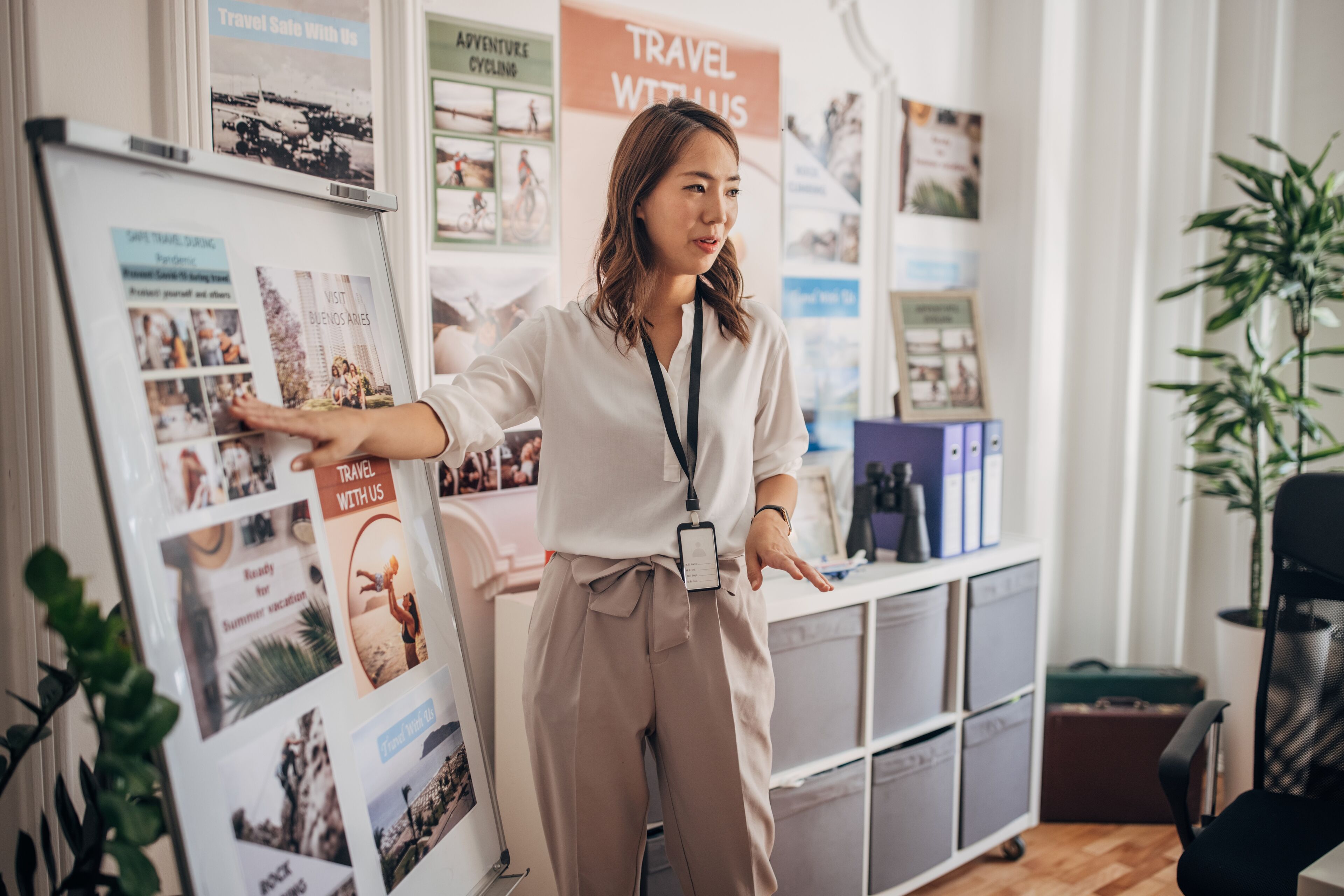 A poised woman presents travel options, pointing to posters in a bright travel agency office.