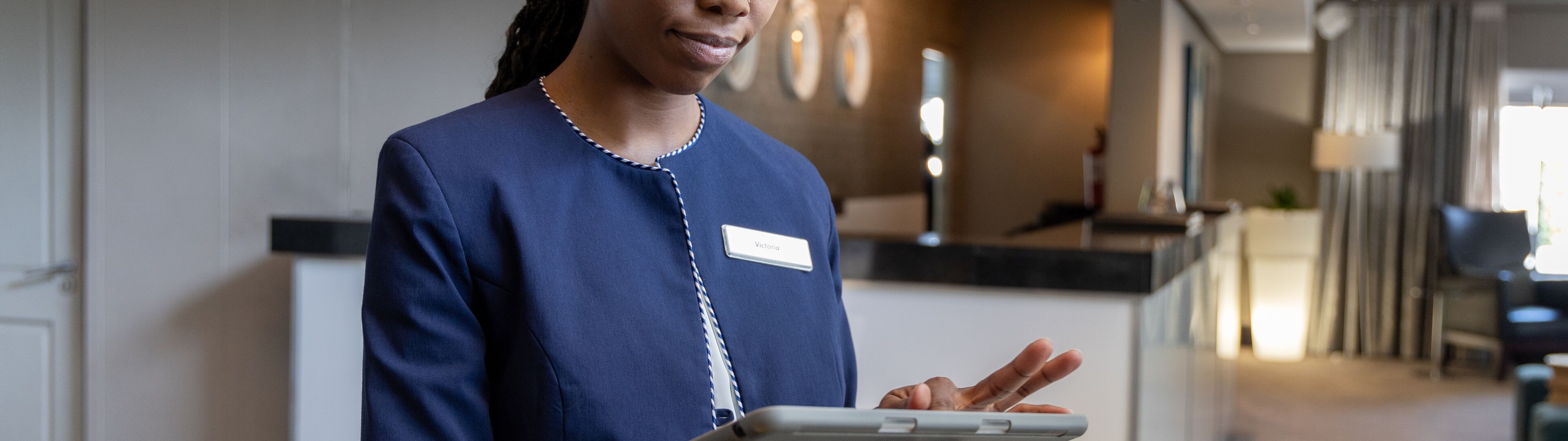 Un employé d'hôtel utilise une tablette, probablement pour gérer les services aux clients ou les enregistrements dans le hall.

