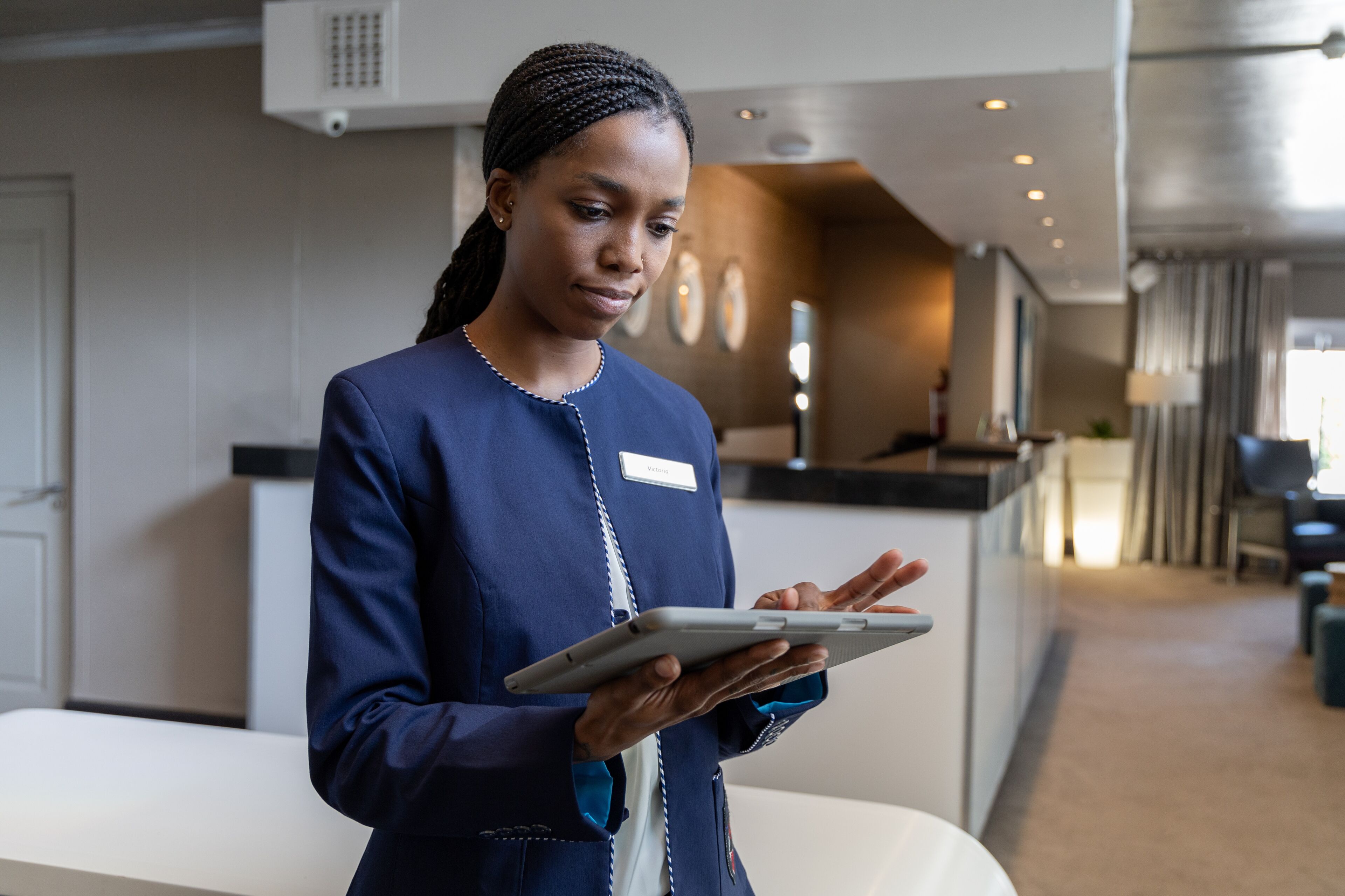 A hotel employee is engaged with a tablet, likely managing guest services or check-ins in the lobby area.

