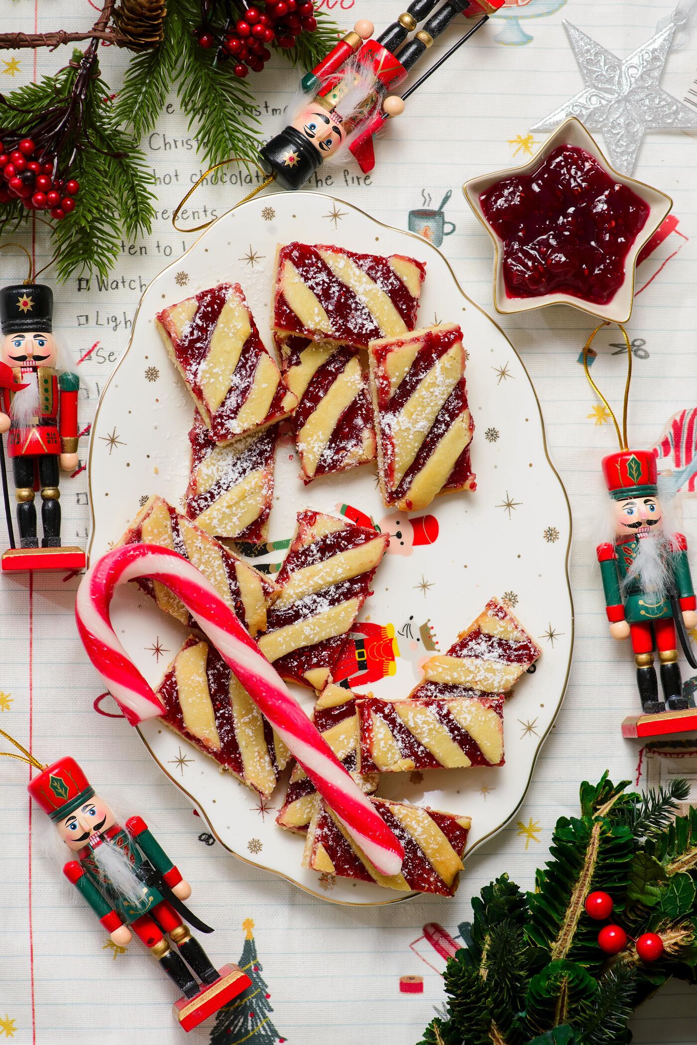 Christmas shortbread cookies with red jam, dusted with powdered sugar and a cookie ribbon. A candy cane and nutcracker decorations are also present.