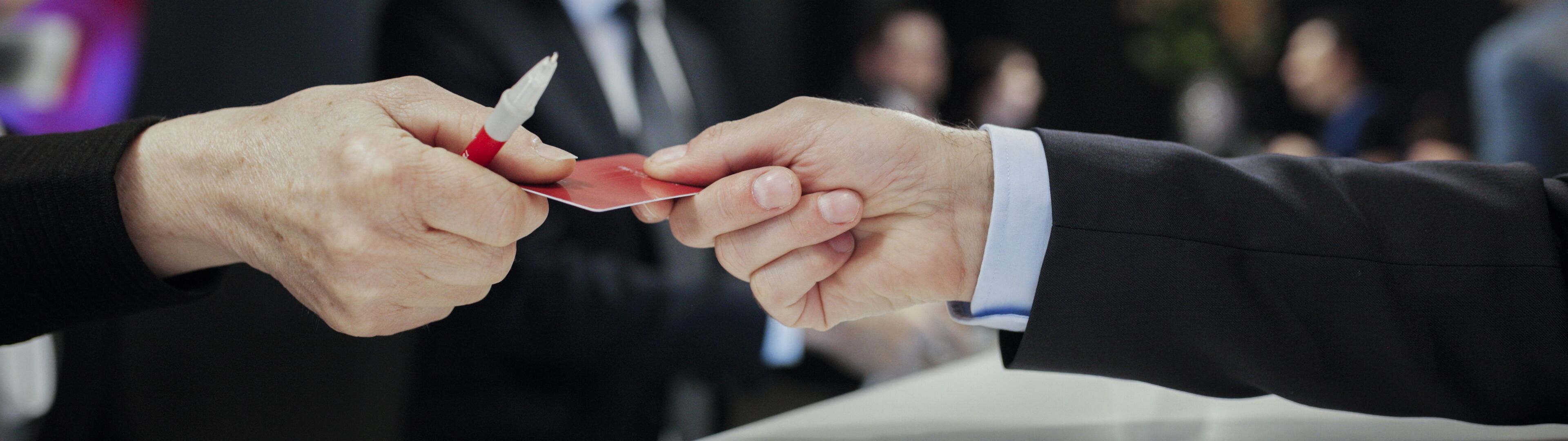 Two professionals exchanging business cards in a blurred conference room setting, signifying a formal introduction or partnership.