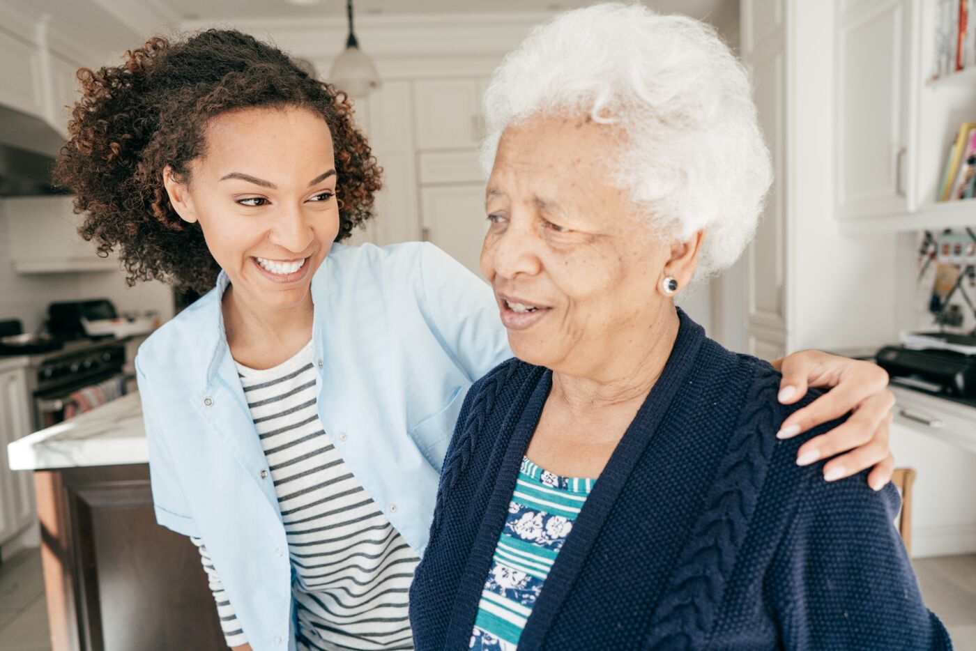 A young woman and her elderly grandmother share a joyful moment in a bright kitchen setting.