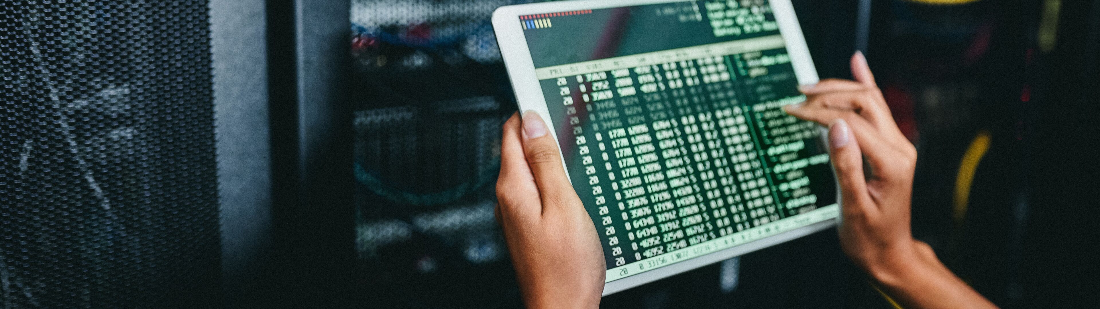 Les mains d'un technicien surveillent l'activité et le diagnostic du réseau sur une tablette numérique, avec une armoire de serveur en arrière-plan.