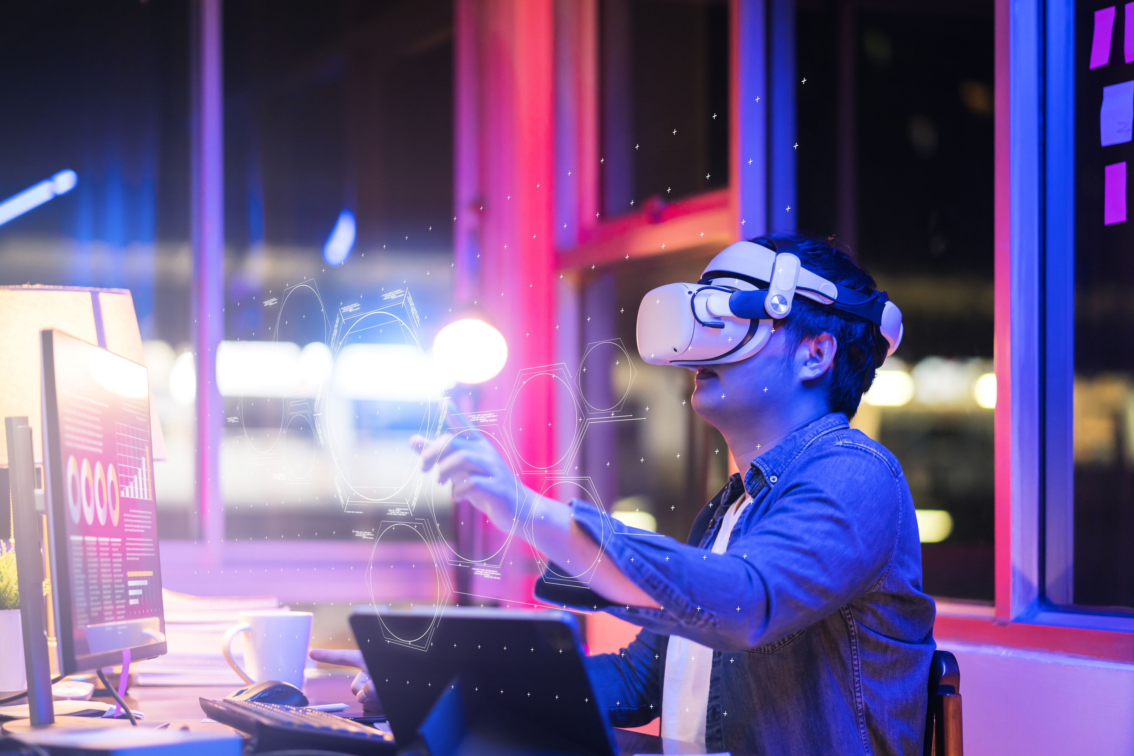 Un homme explore un environnement virtuel avec un casque VR, entouré de graphiques numériques, dans un bureau moderne illuminé par des lumières néon colorées la nuit.