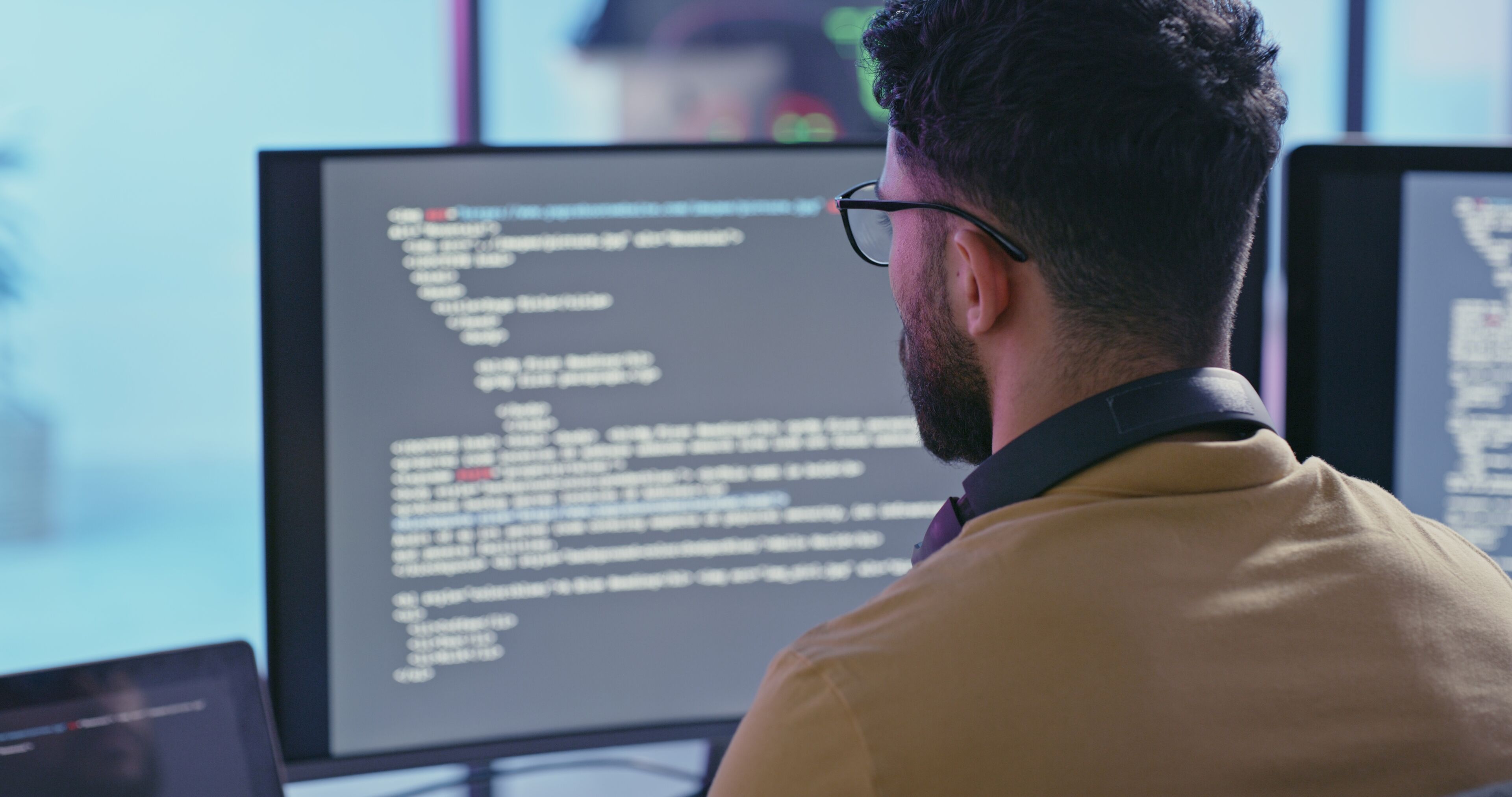 Un programmeur se concentre intensément sur le code sur des écrans doubles dans un environnement technologique moderne.