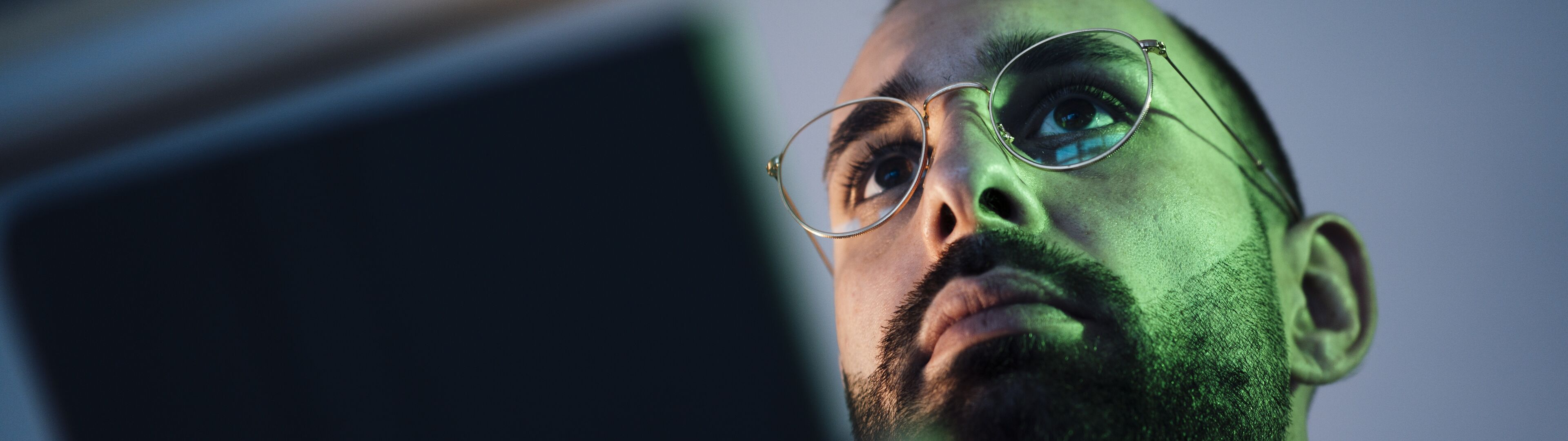 Gros plan d'un homme à lunettes regardant un appareil portable, avec la lumière de l'écran se reflétant sur son visage.


