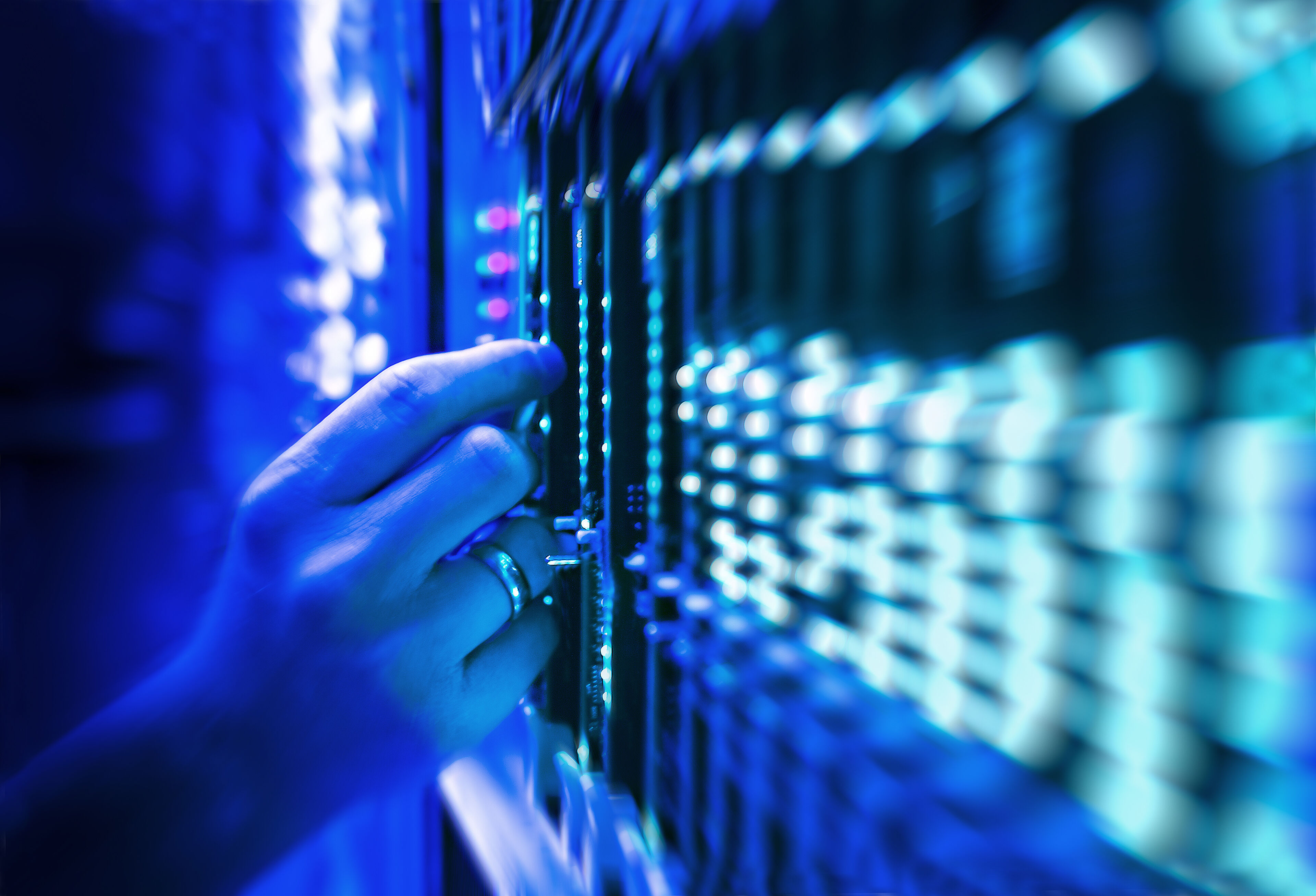Main d'un technicien insérant de l'équipement dans un rack serveur dans un centre de données éclairé en bleu.