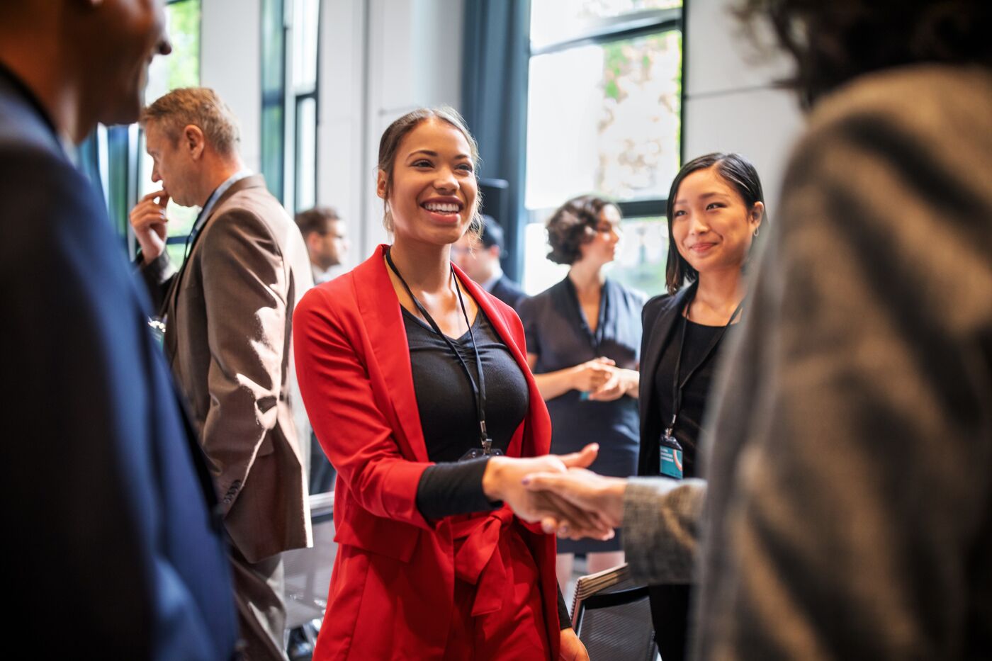 Two women engaging in a handshake at a professional networking event, with attendees in the background.