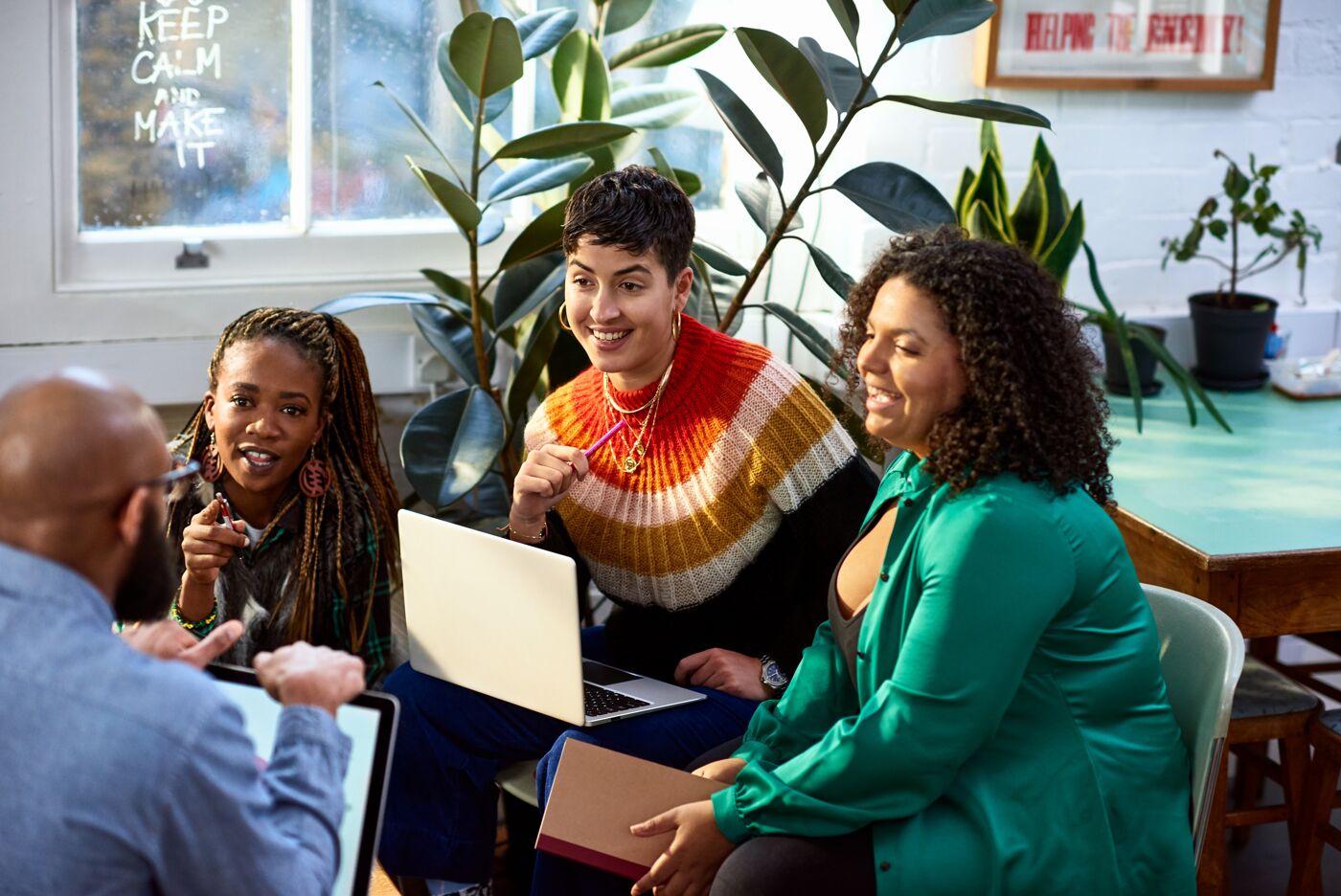 Four professionals engage in a lively discussion in a bright, plant-filled office space.