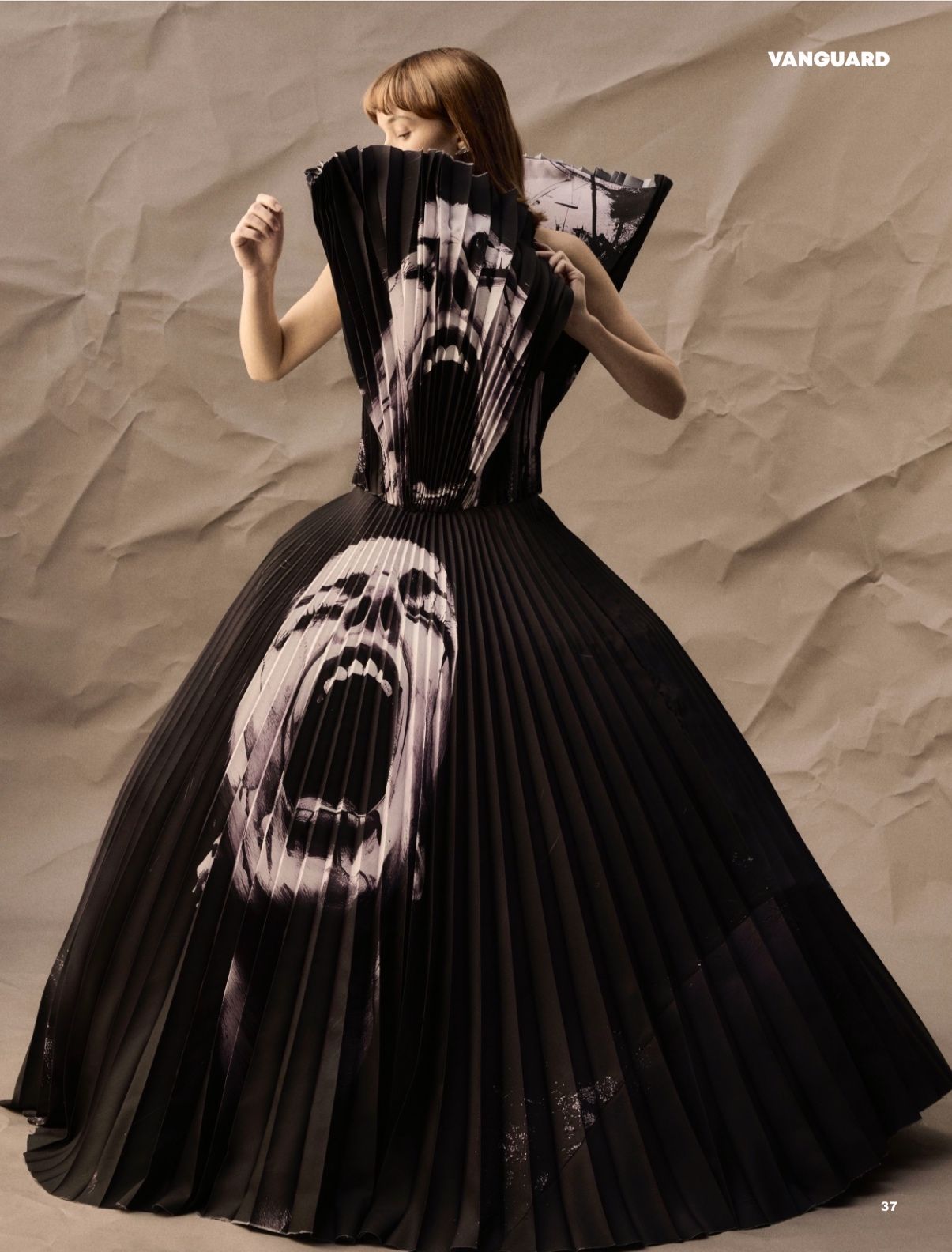 A black gown featuring a screaming face design in black and white, with a pleated collar and skirt. The image has a crumpled paper background.