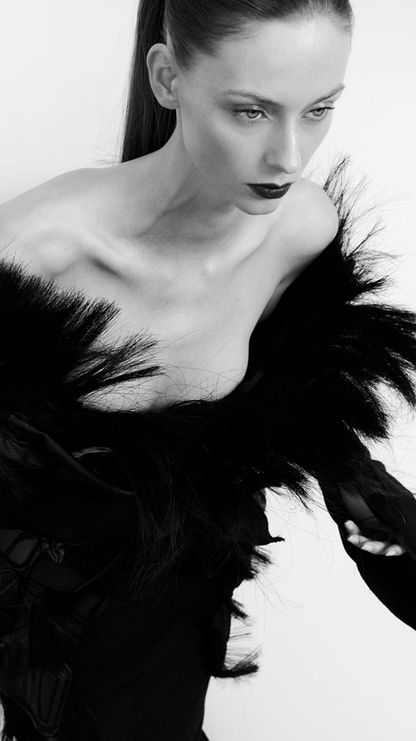 A woman in a black feathered dress, with her hair in a high ponytail, looks to the right with dramatic makeup.