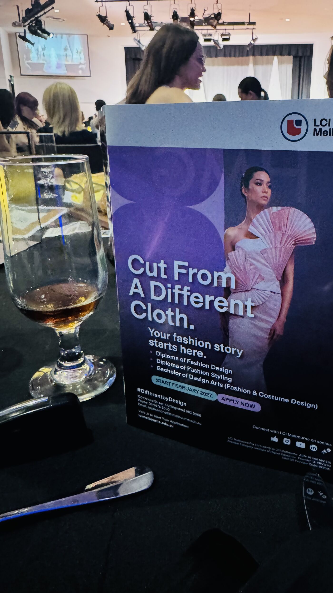 This image shows a table tent card from LCI Melbourne, a fashion design school, with the tagline "Cut From A Different Cloth. Your fashion story starts here." It features a model in a stylish outfit.