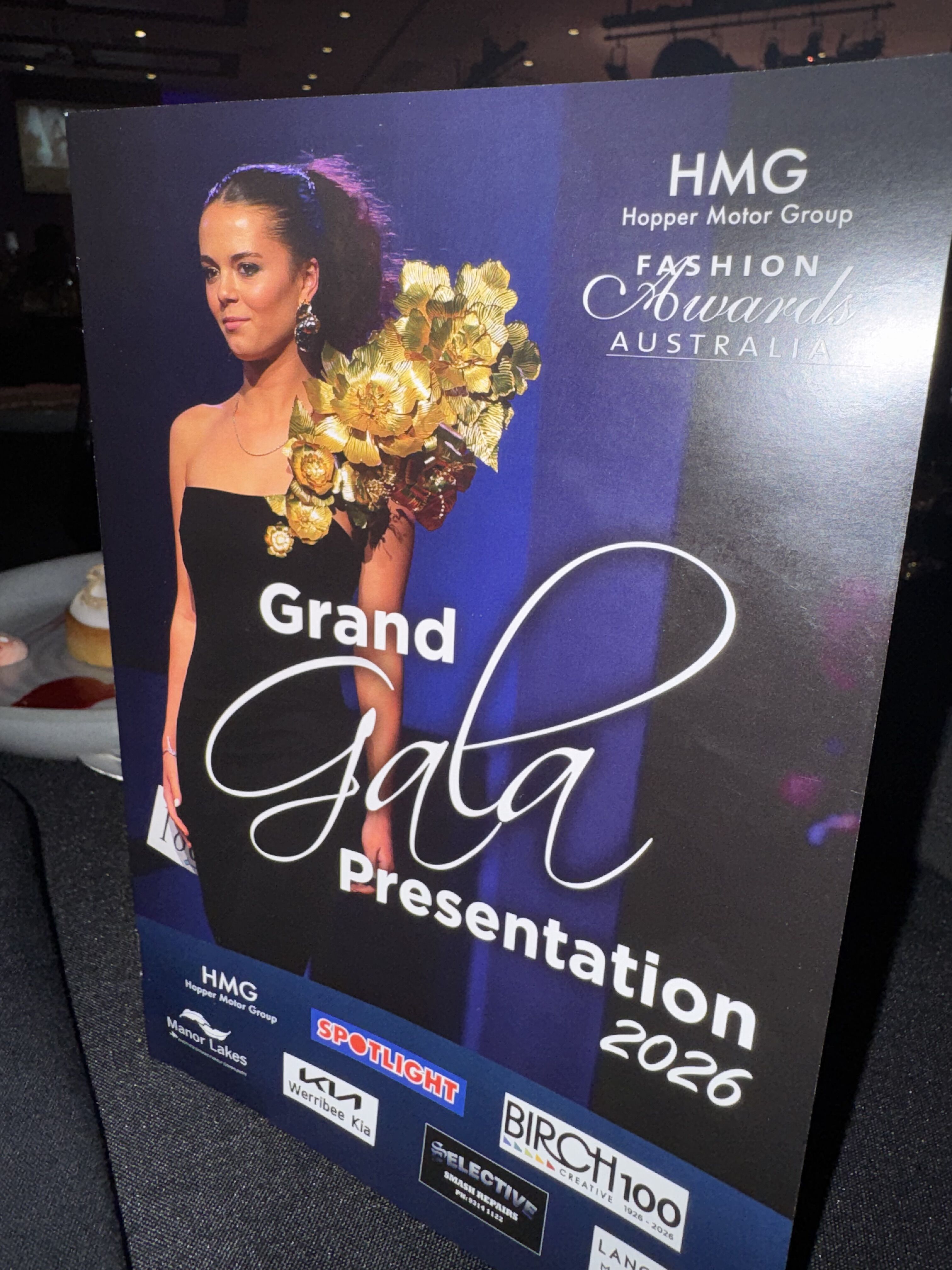 This image shows a poster for the HMG Hopper Motor Group Fashion Awards Grand Gala Presentation in 2026. It features a woman in a black dress and highlights various sponsors.