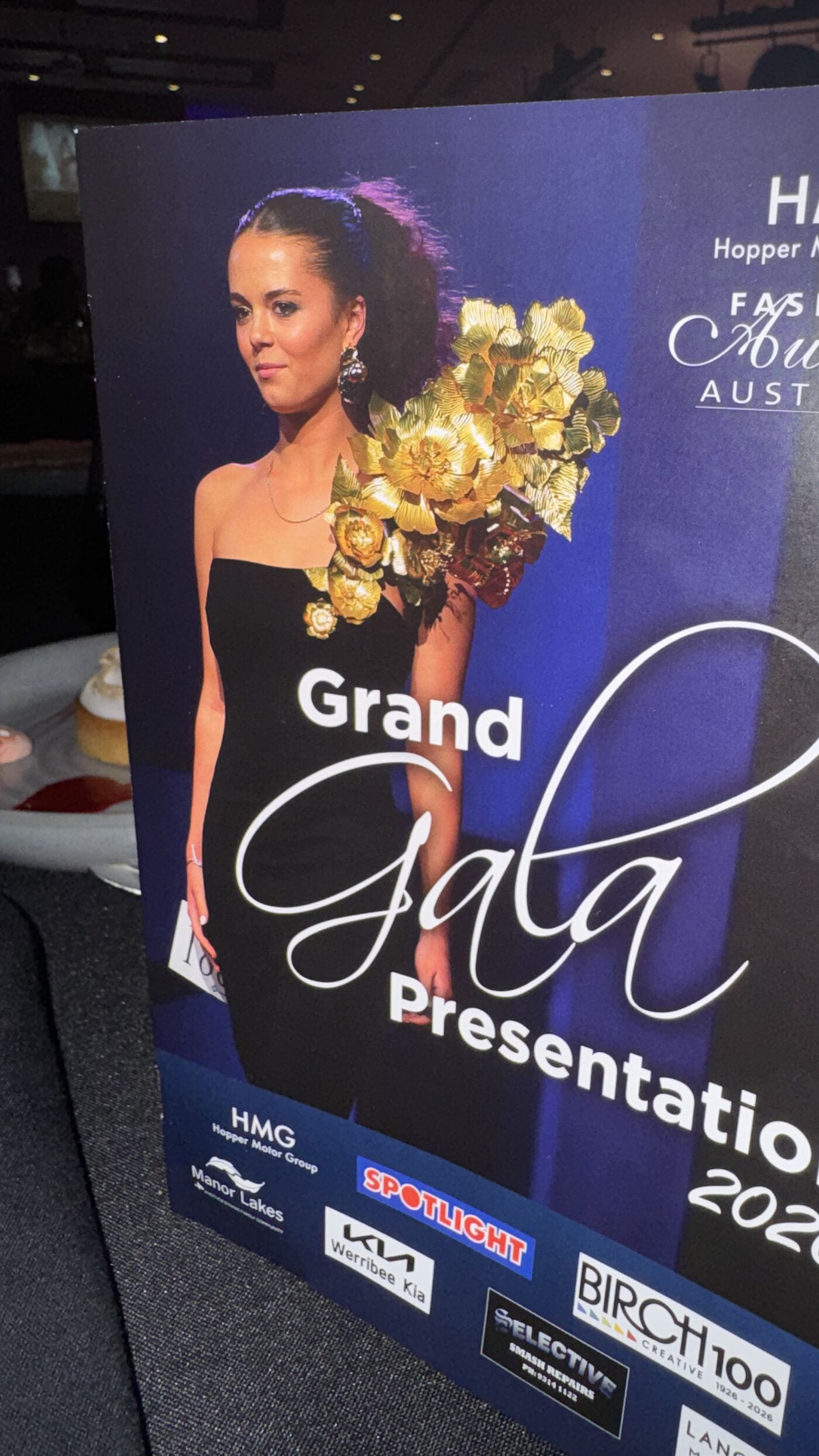 This image shows a poster for the HMG Hopper Motor Group Fashion Awards Grand Gala Presentation in 2026. It features a woman in a black dress and highlights various sponsors.