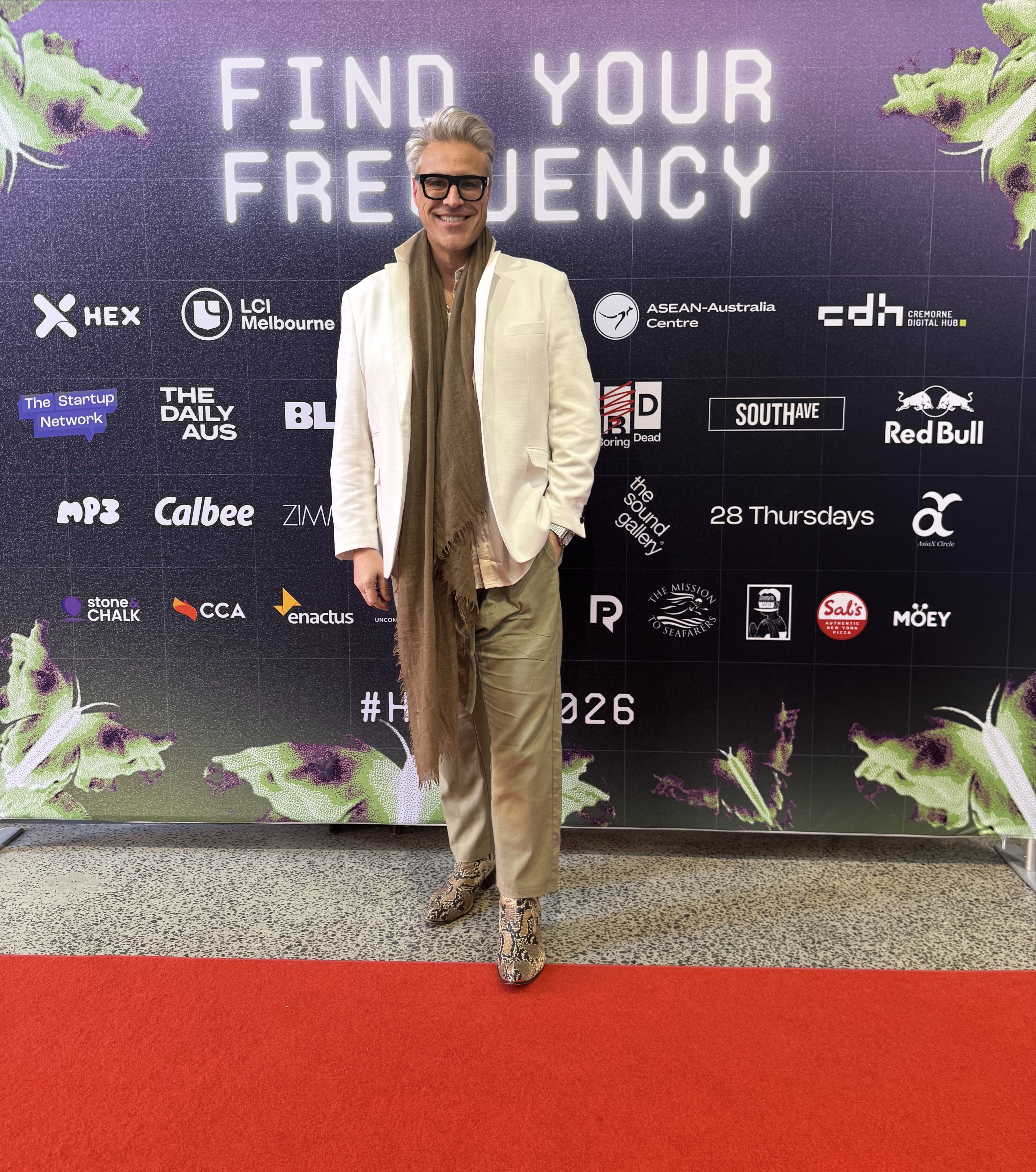 A man in a white jacket and brown scarf stands in front of a wall with the slogan "FIND YOUR FREQUENCY".