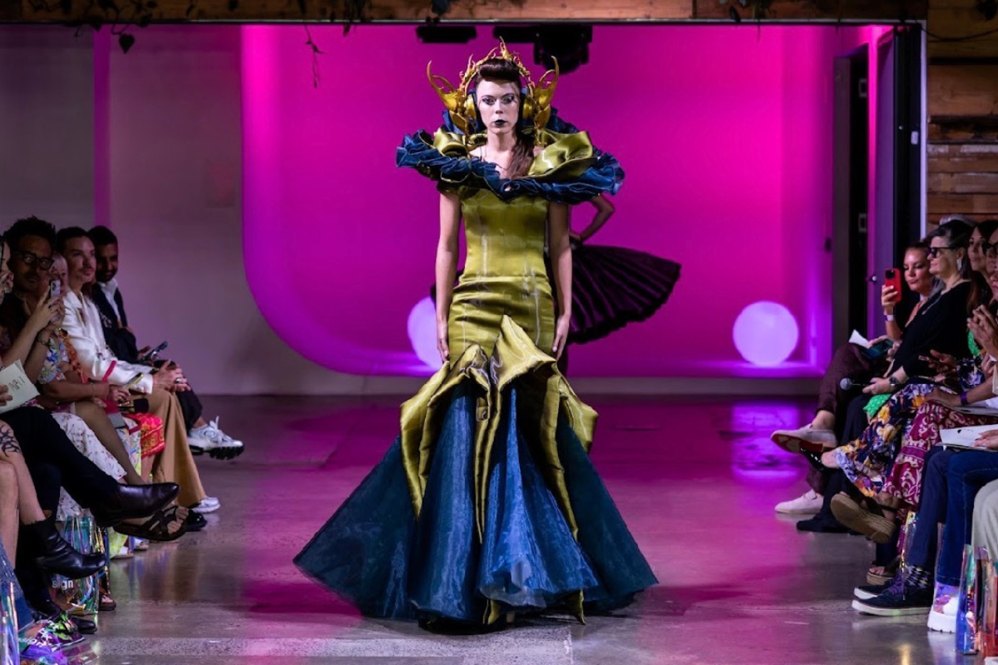 A model showcases an avant-garde gown on a runway. The dress features a unique design with bold colors and intricate details, captivating the audience.