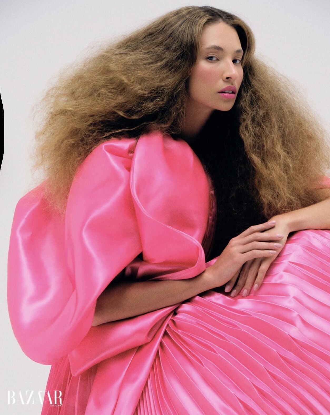 A woman with long, voluminous curly hair and a vibrant pink dress poses for a fashion photoshoot, exuding elegance and confidence.