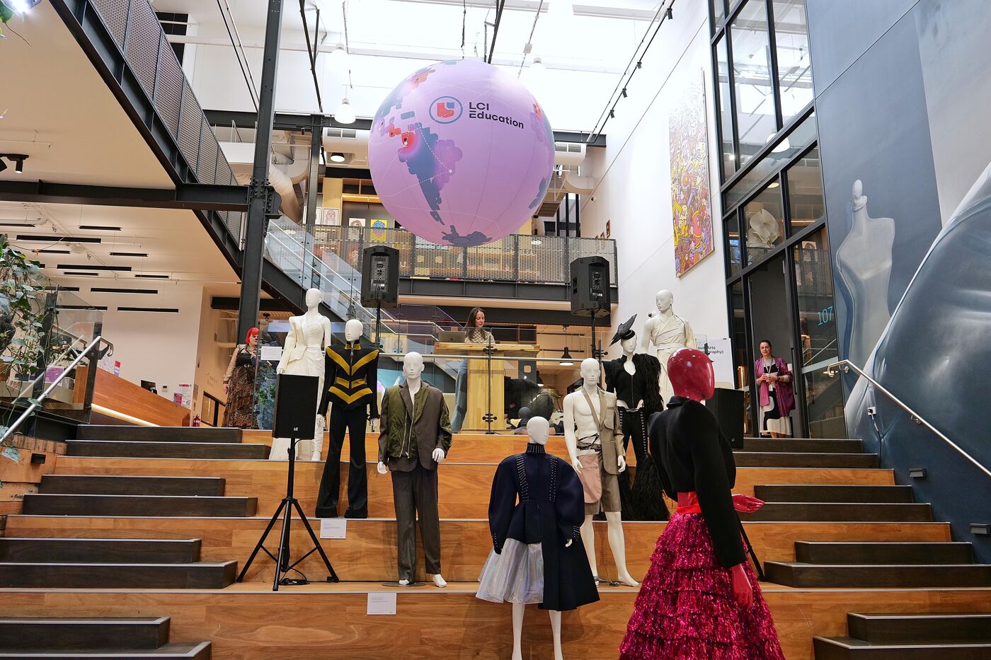 A large inflatable globe with a world map hangs from a high ceiling, with mannequins wearing outfits on the stairs below.
