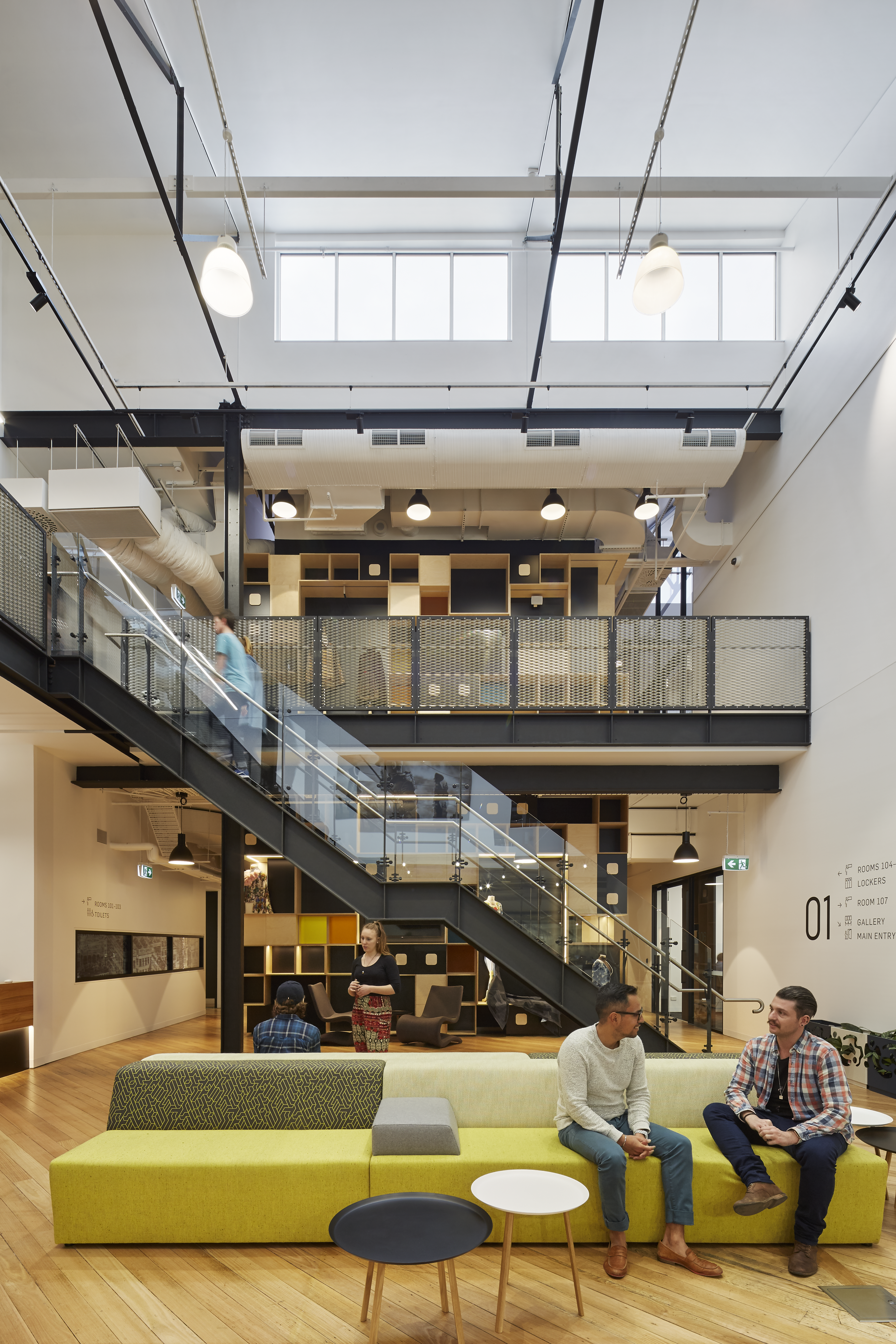 Colleagues converse in a spacious, well-lit open-plan office with stairs connecting multiple levels.