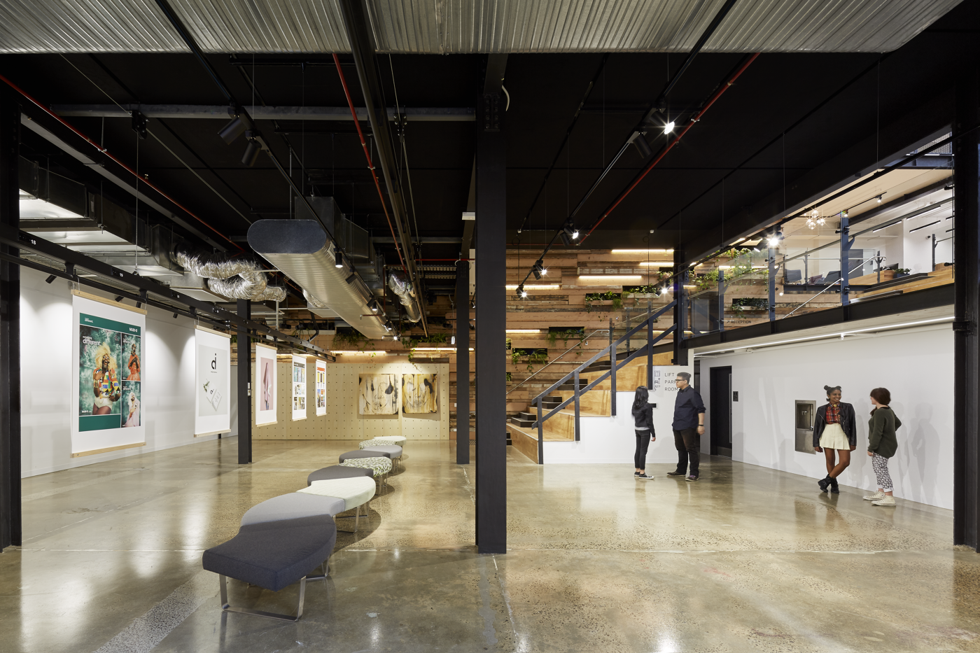 Visitors stroll through an art gallery with an industrial chic aesthetic and a grand staircase.