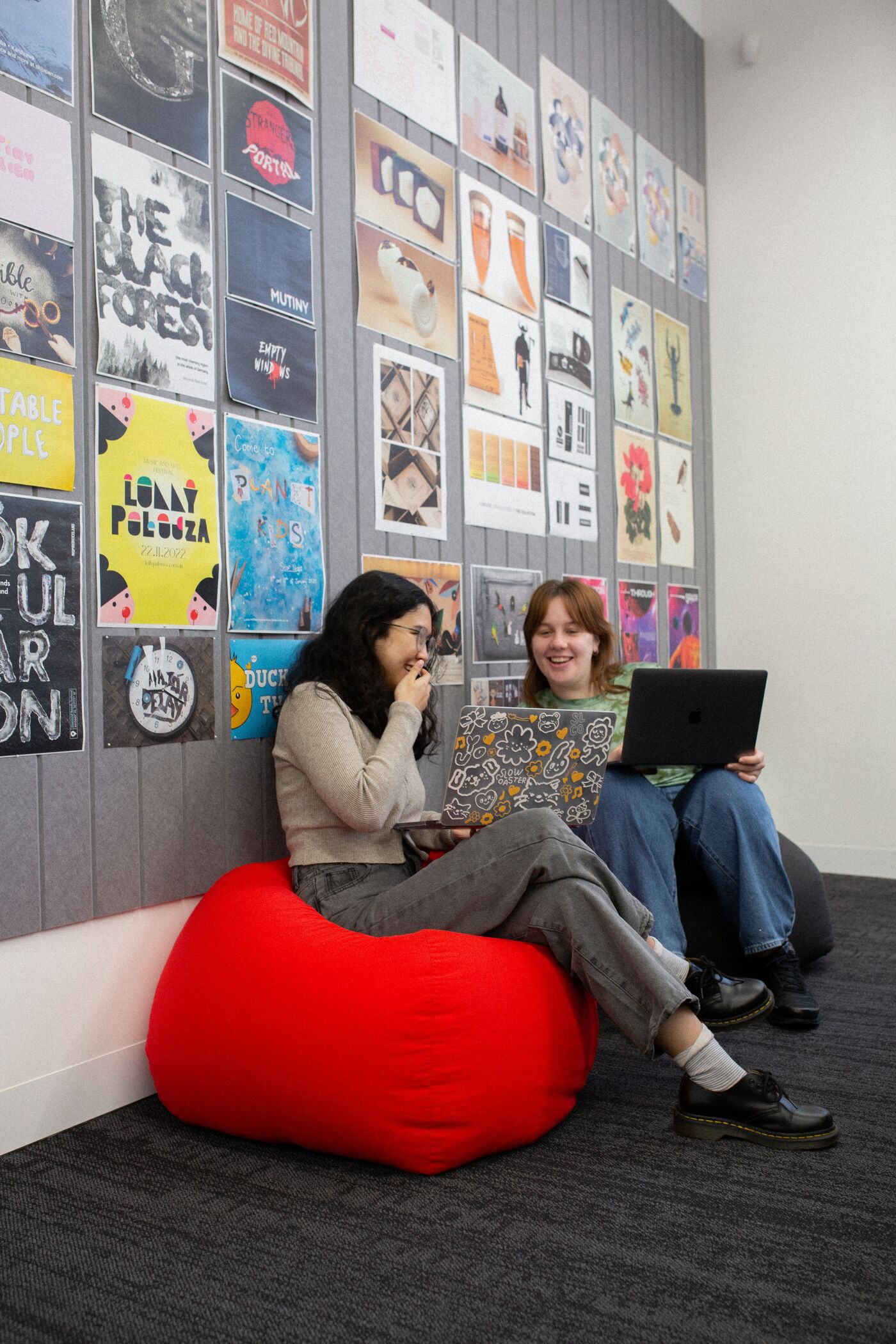 Two students laugh and share ideas on a red beanbag in a vibrant campus lounge.
