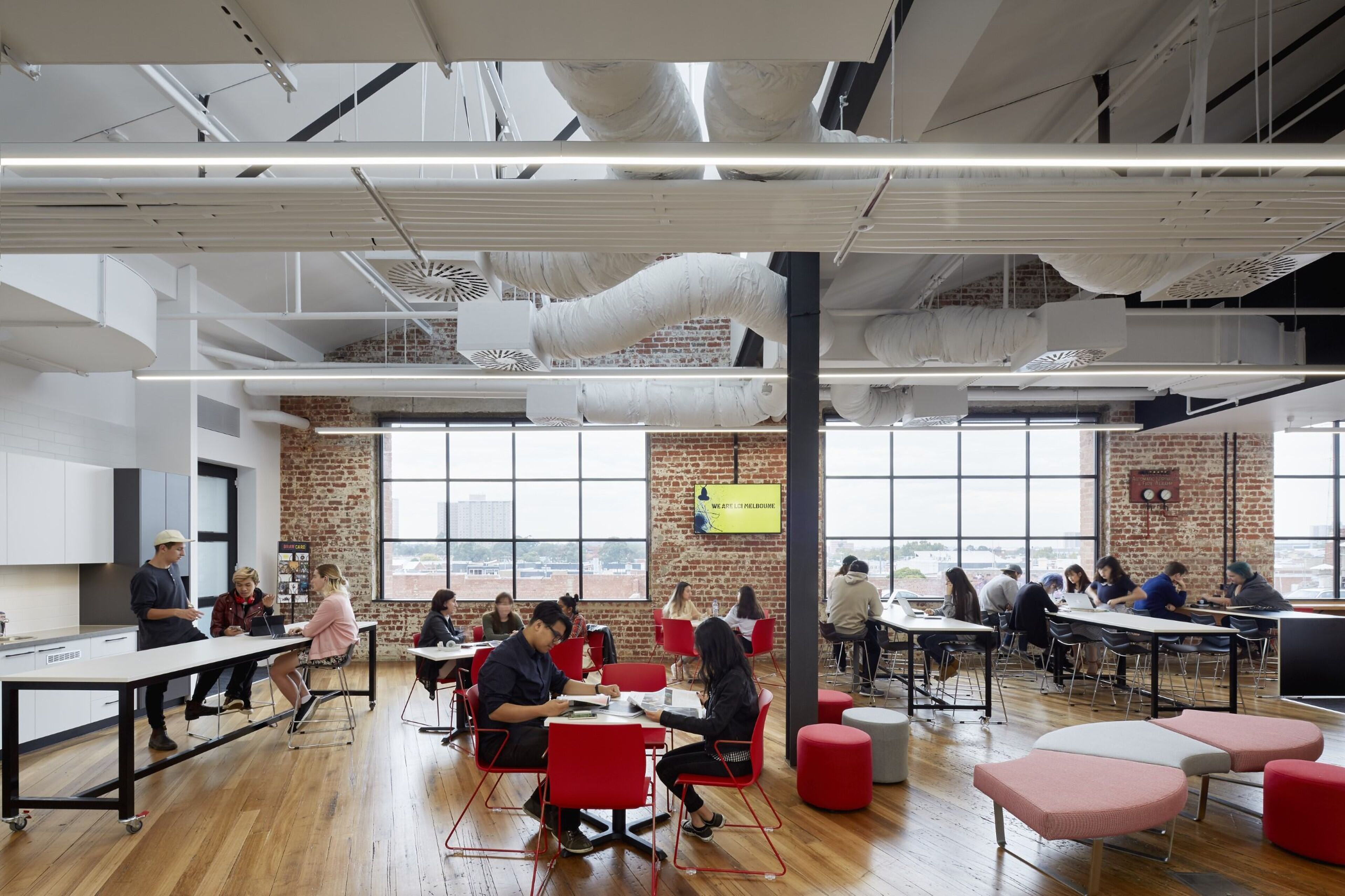 Students study and collaborate in a stylish, brick-walled communal space with large windows.