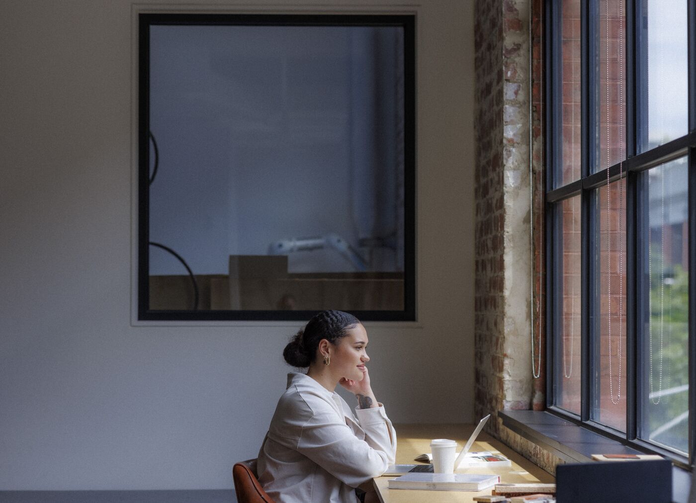 A focused individual sits by the window, immersed in thought, surrounded by the quiet ambience of a serene workspace.