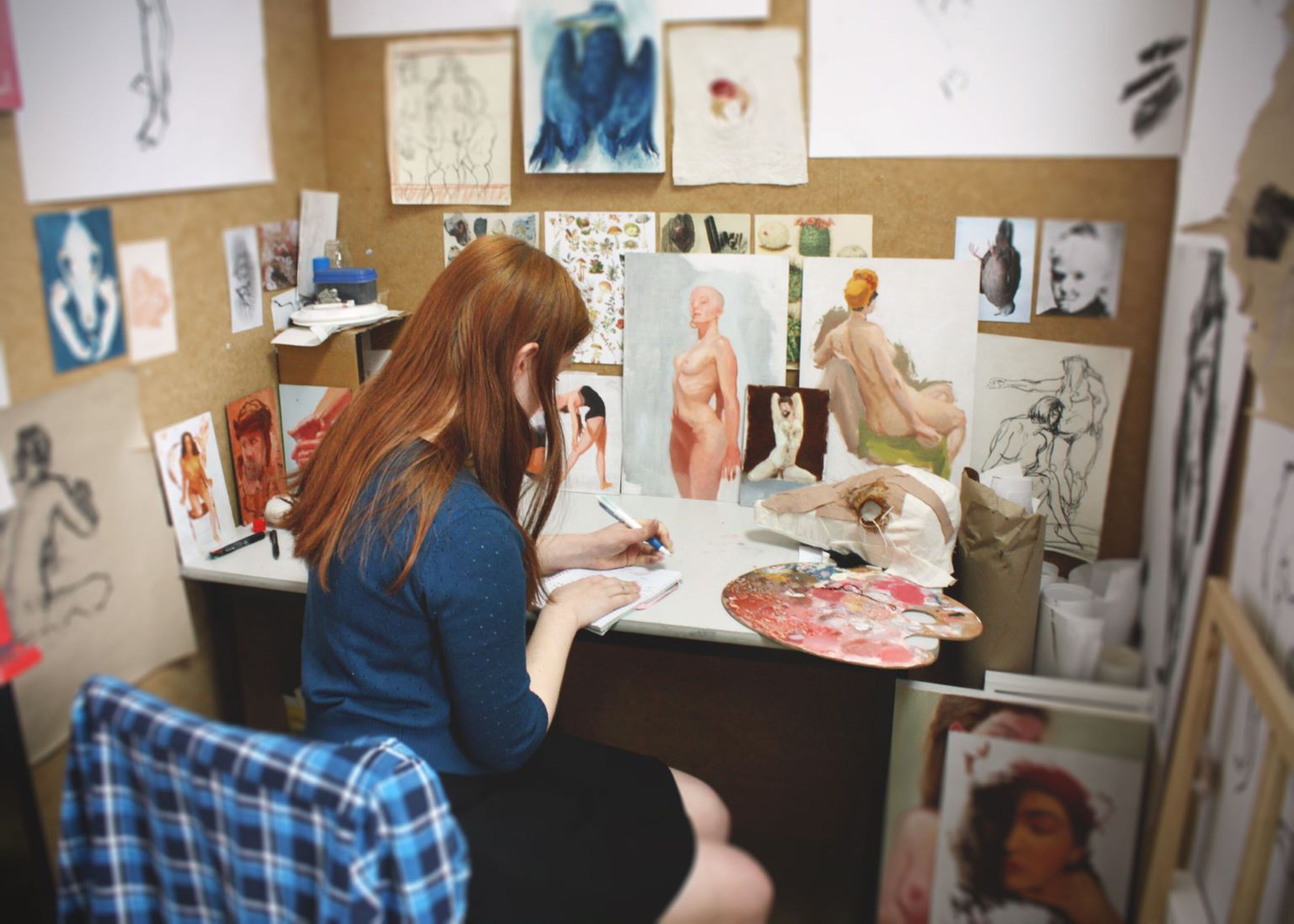 An artist lost in concentration sketches in her studio, her fiery hair mirroring the passion of her work.