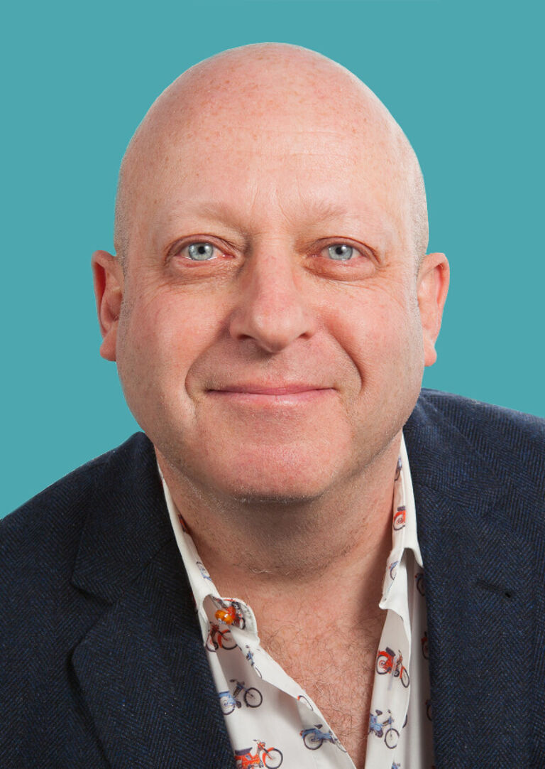 A bald, middle-aged man sporting a friendly smile, wearing a navy jacket over a shirt with bicycle prints.