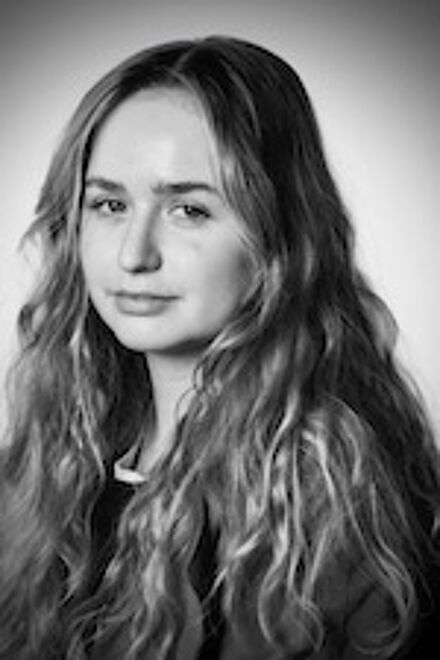 A portrait of a young woman with long, wavy hair, gazing intently. The photo's monochrome tone highlights her features.