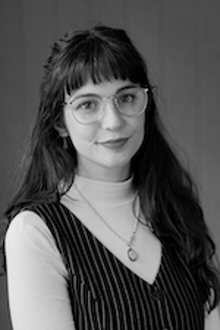 A monochrome portrait of a content young woman wearing glasses and a sleeveless striped top, exuding a subtle charm.