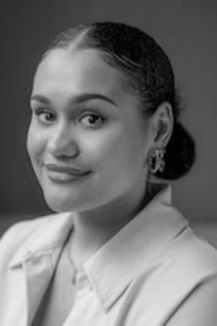 A black and white portrait of a smiling woman with pulled-back hair, wearing earrings and a light shirt, exuding confidence.