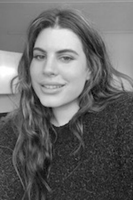 A cheerful woman with wavy hair and a knitted sweater poses for a black-and-white photograph.