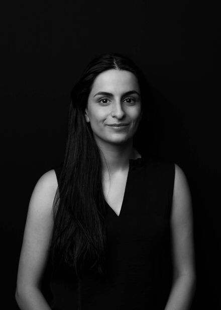 A monochrome portrait of a woman with long hair, smiling subtly against a dark background.