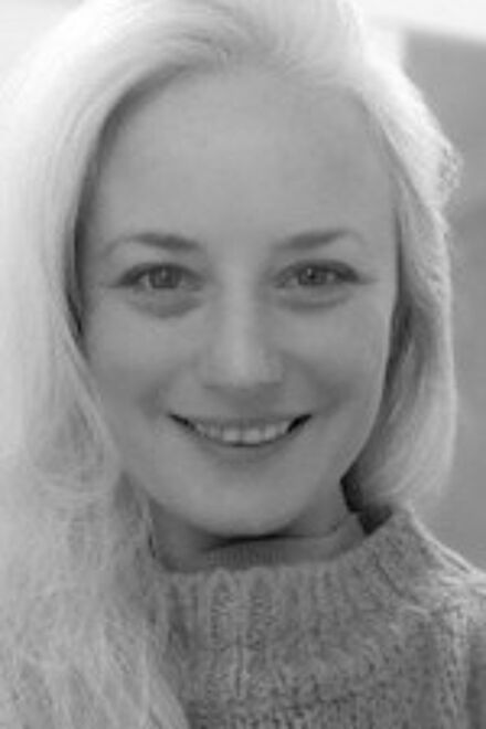 Black and white close-up photo of a smiling woman with blonde hair, wearing a knit sweater.