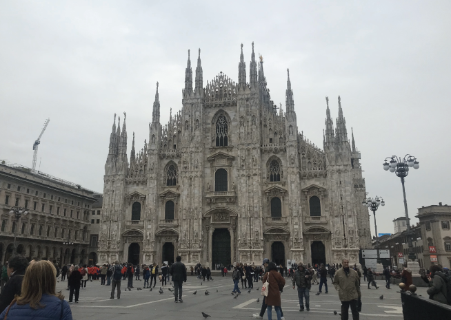 The majestic Milan Cathedral (Duomo di Milano) with its Gothic architecture dominates Piazza del Duomo, surrounded by tourists.